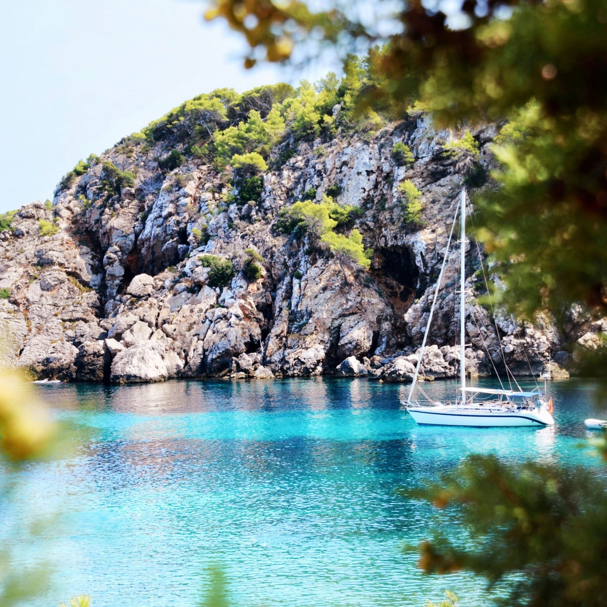 White sailboat in clear turquoise rocky cove with green cliffs.