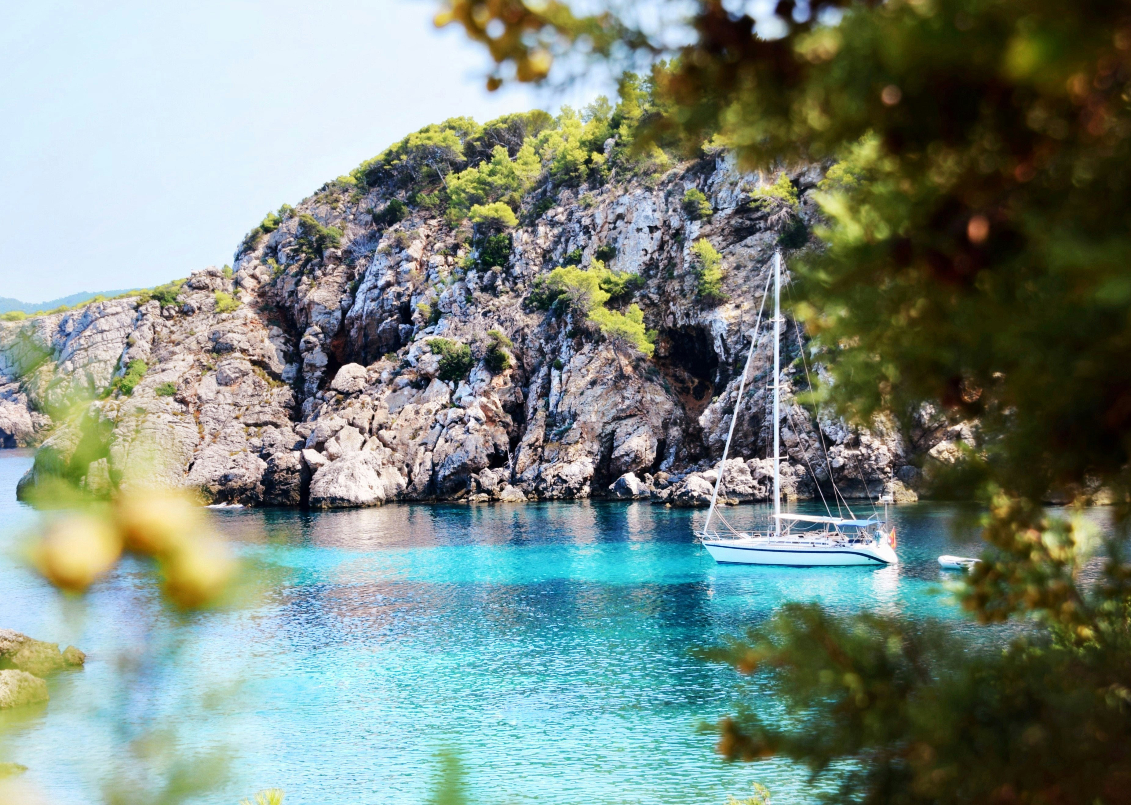 White sailboat in clear turquoise rocky cove with green cliffs.