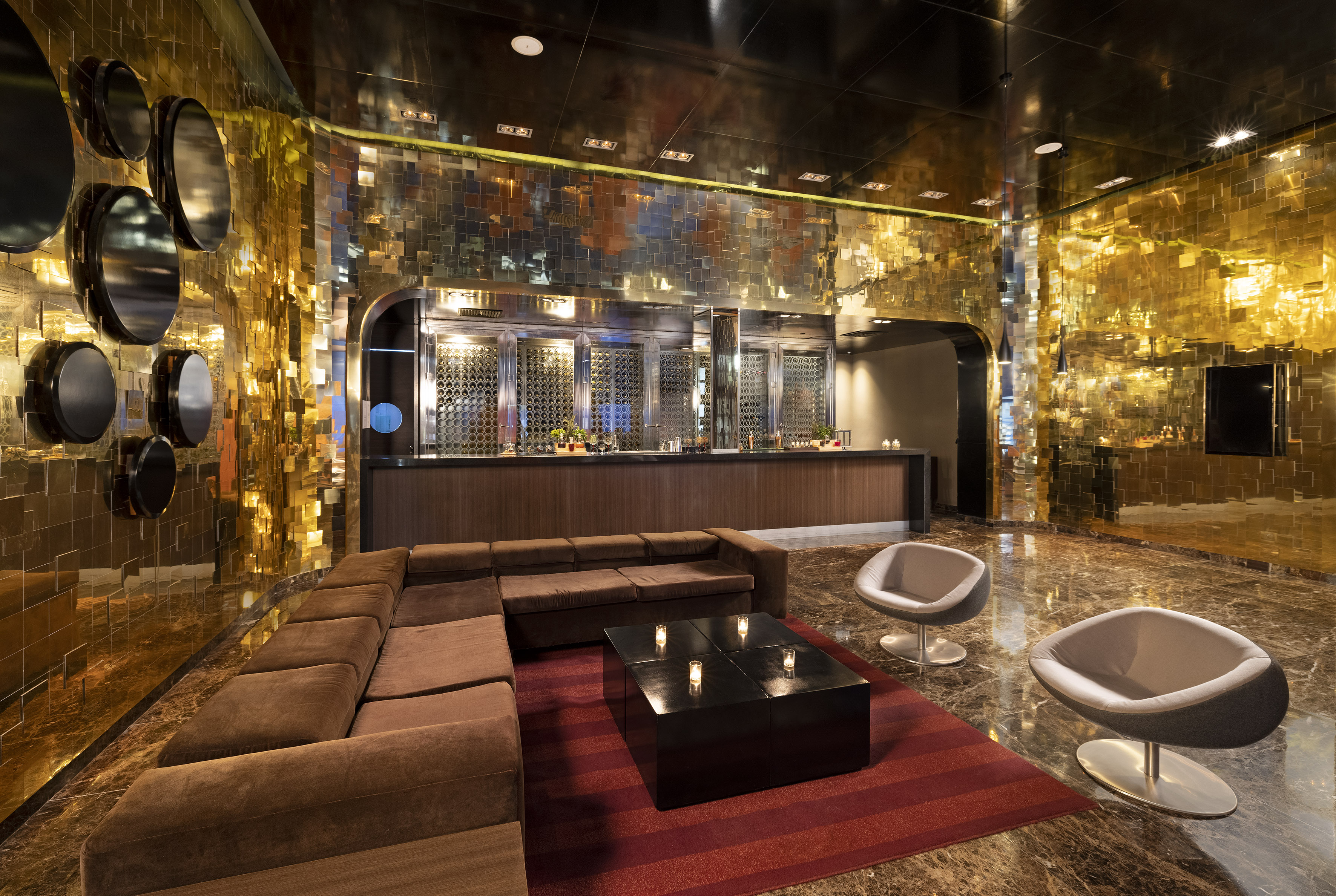 Luxurious hotel lounge with golden textured walls, brown sofa, and modern bar.
