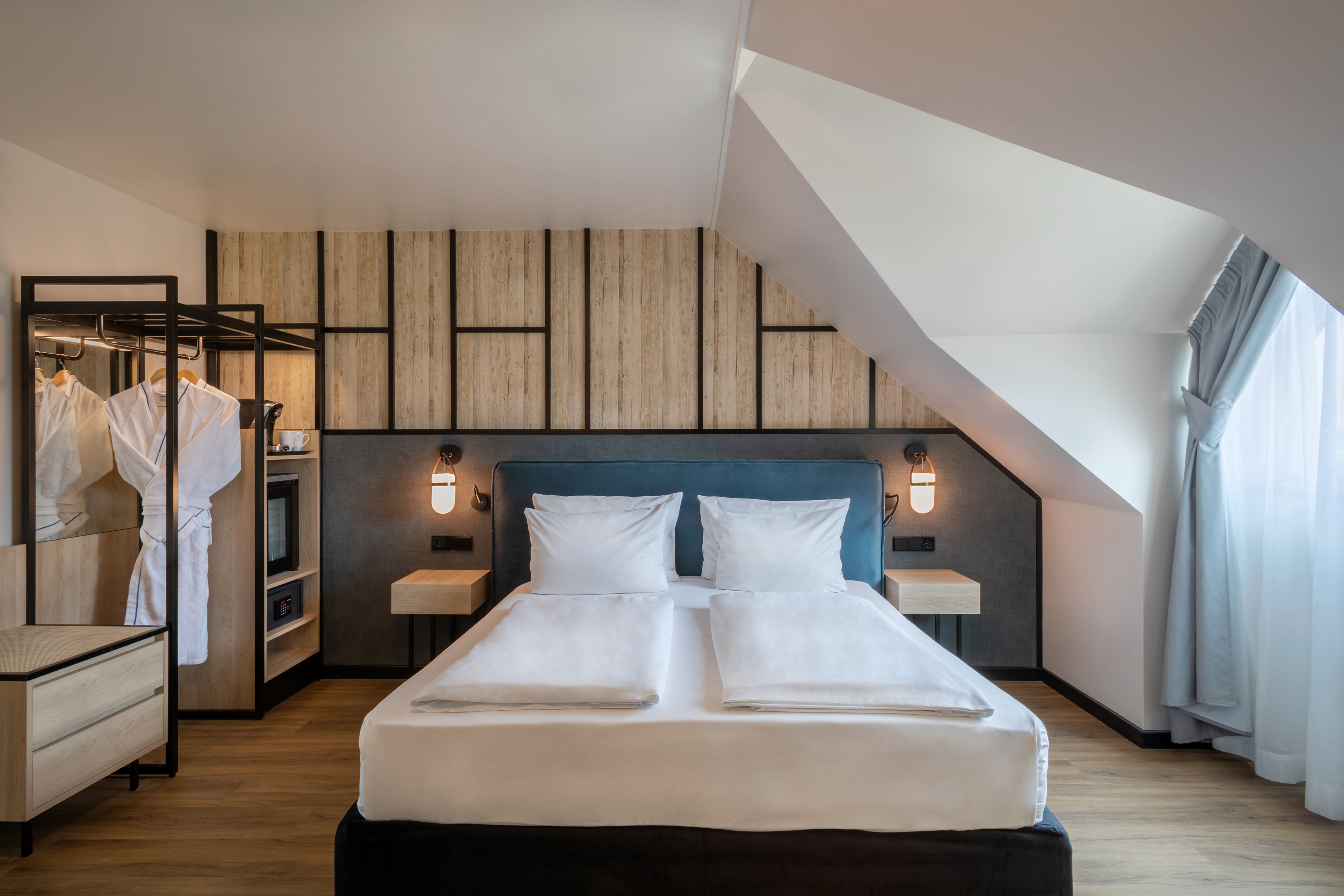 Modern hotel room with cozy bed, wood accents, and sloping ceiling.