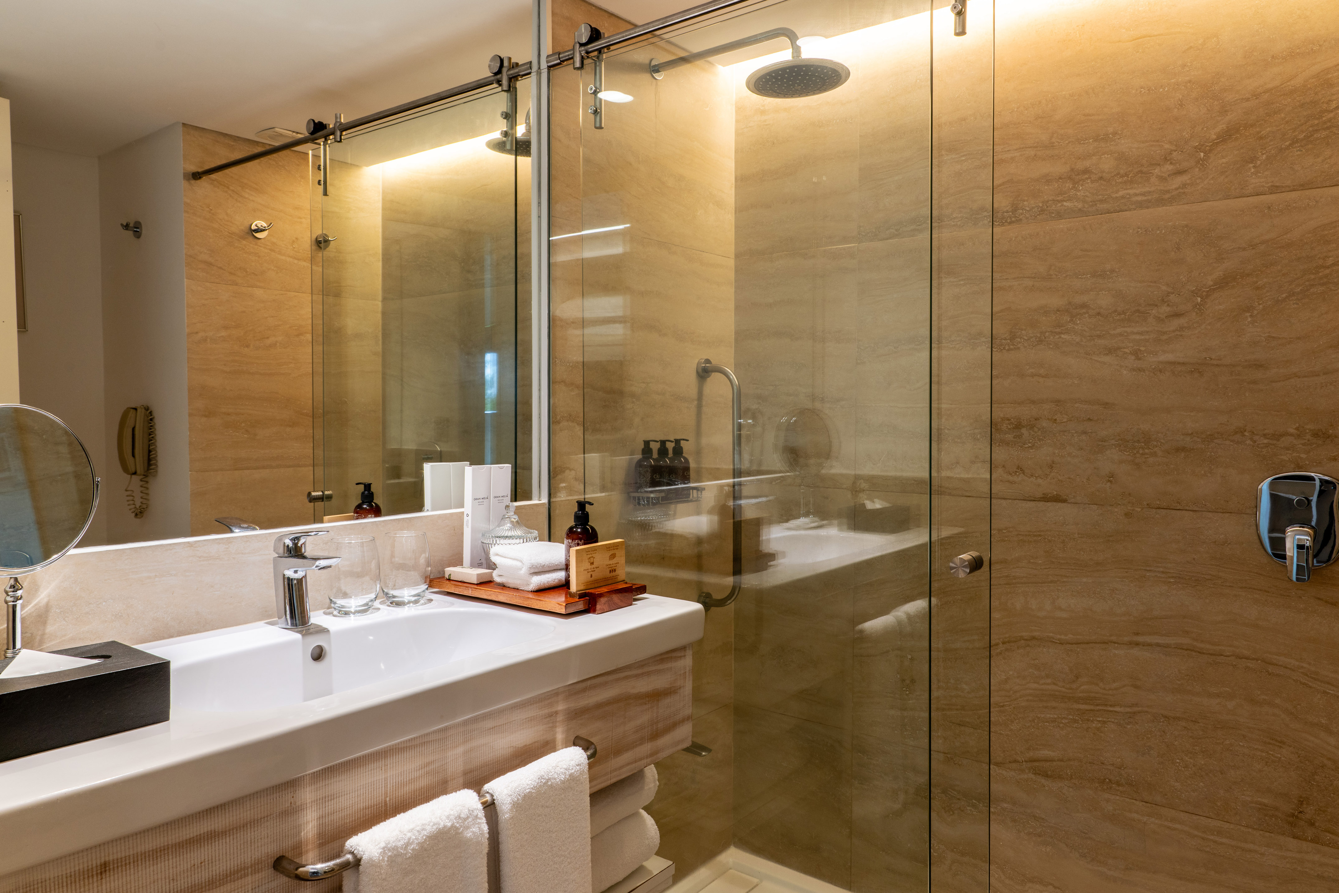 Luxury hotel bathroom with modern vanity, glass shower, and marble-look tiles.
