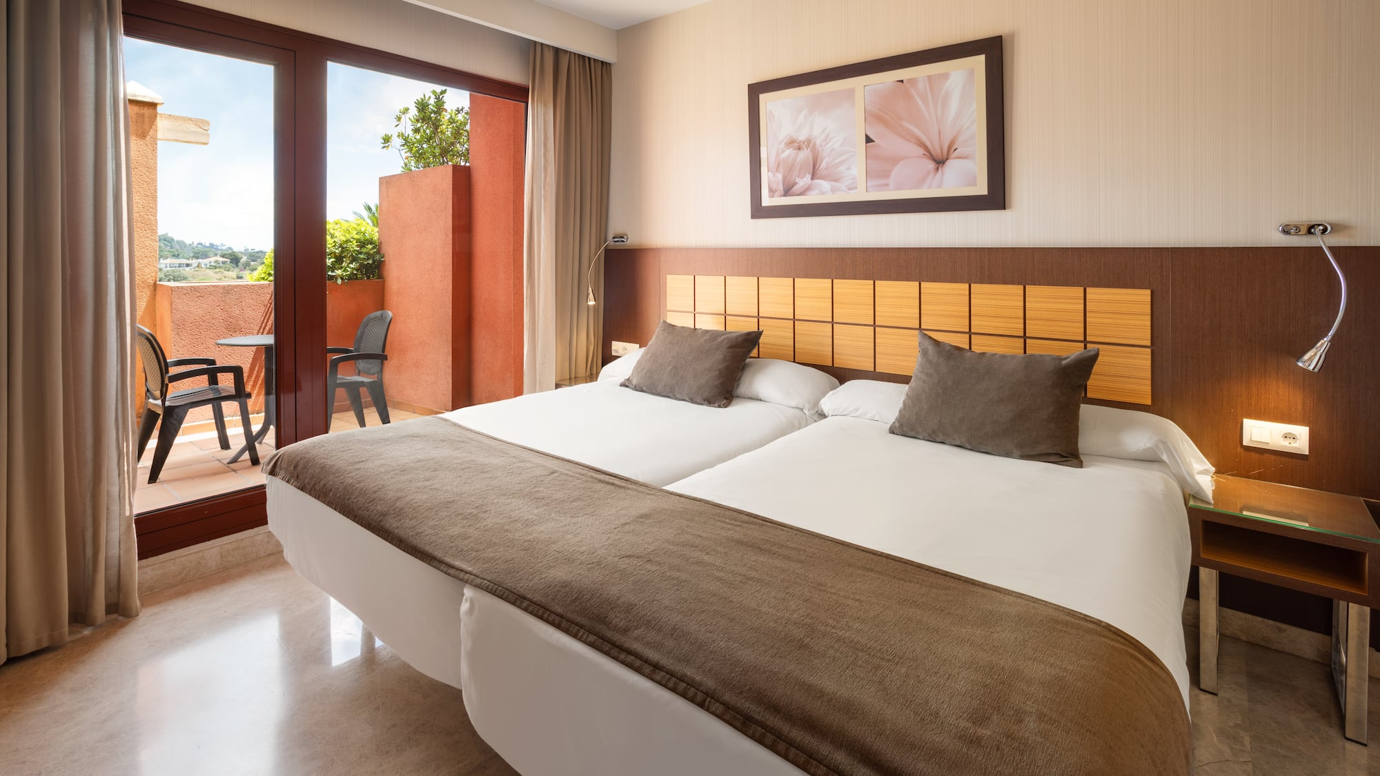 Hotel twin room with balcony, two beds, and outdoor seating area.