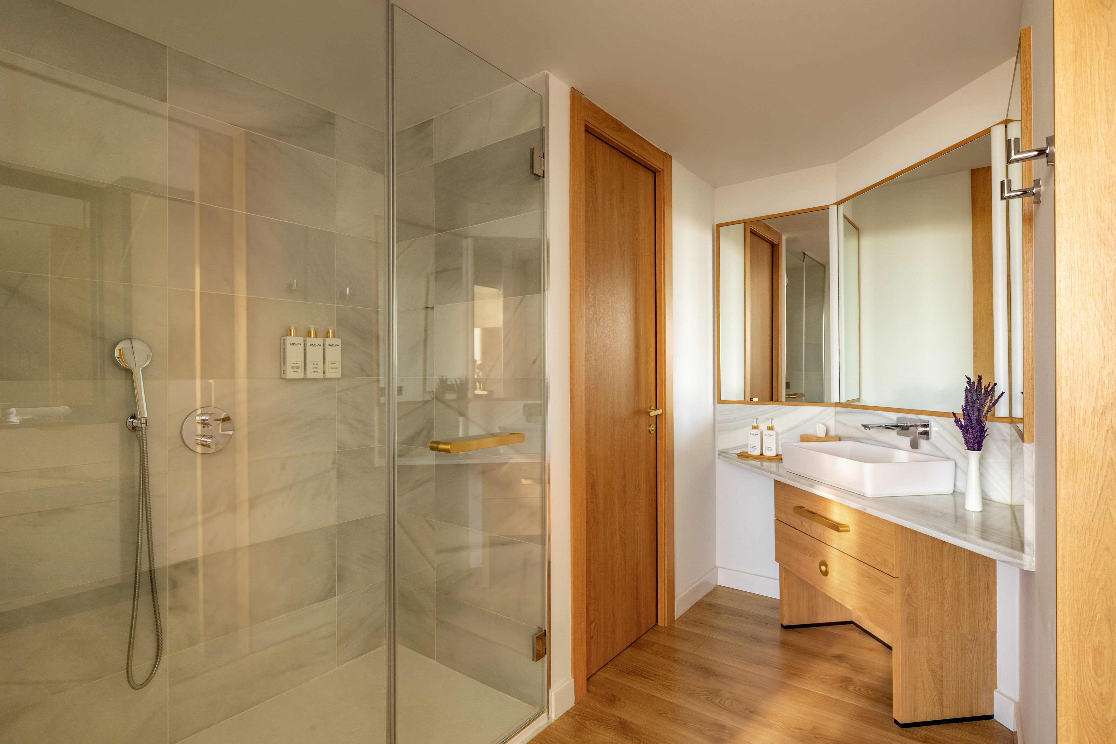 Modern bathroom with glass shower, marble tiles, wood vanity, and gold accents.