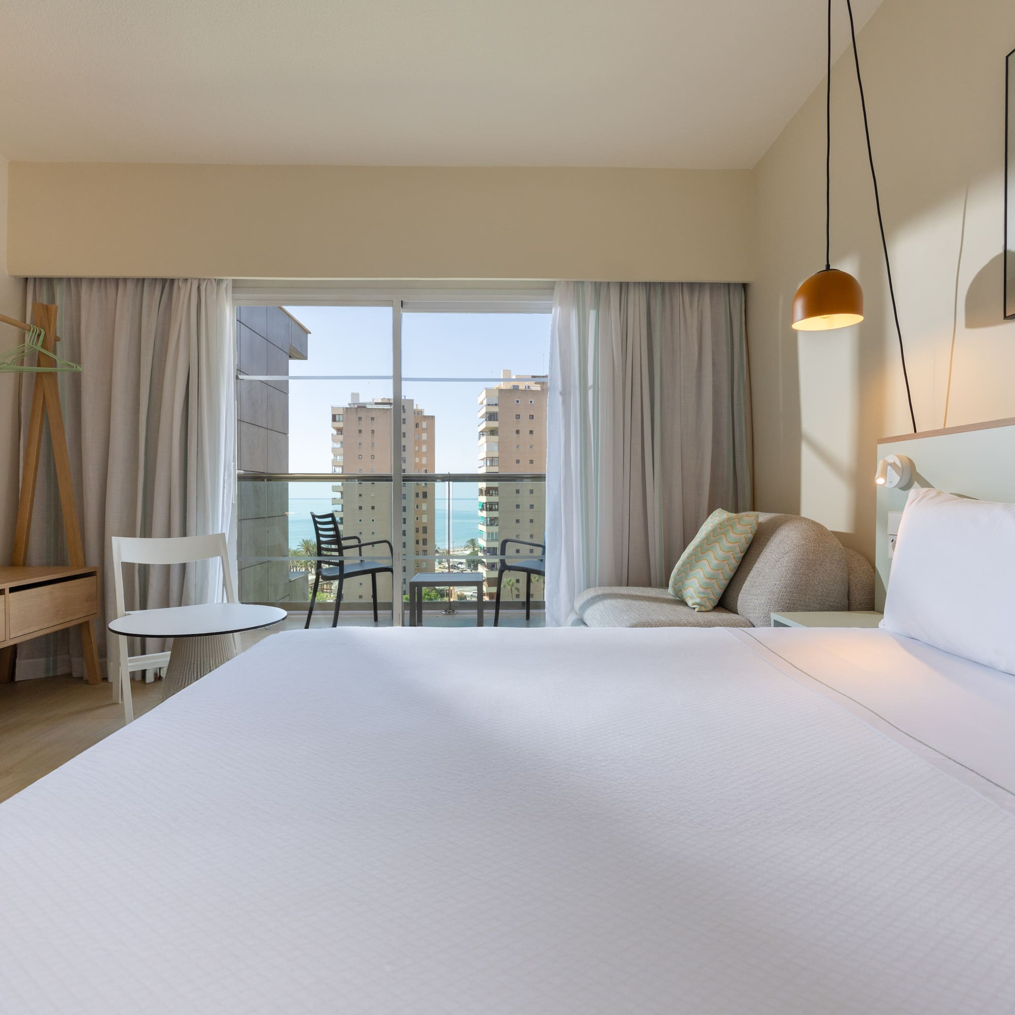 Modern hotel room with ocean view balcony, large bed, and contemporary decor.