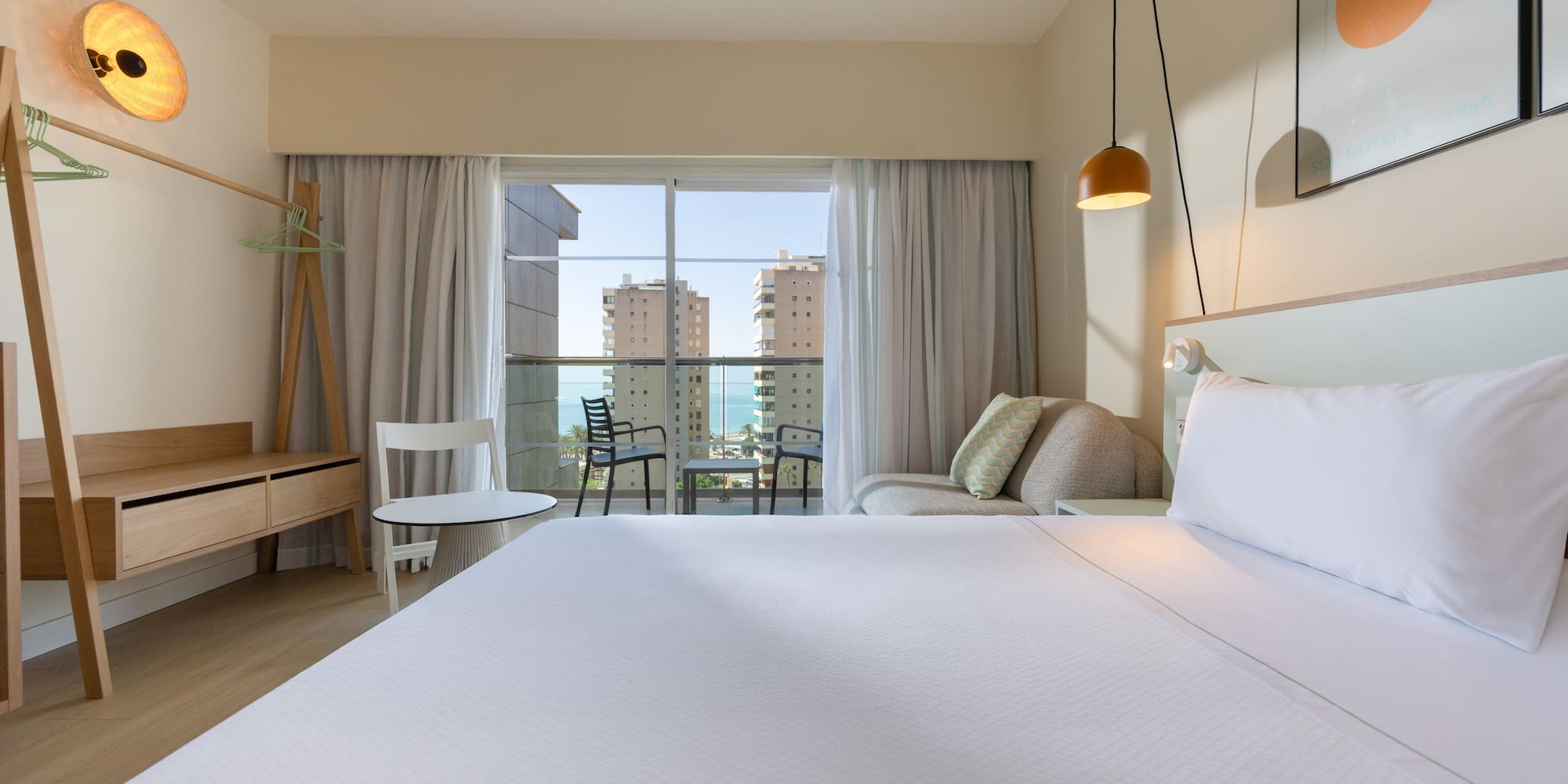 Modern hotel room with ocean view balcony, large bed, and contemporary decor.