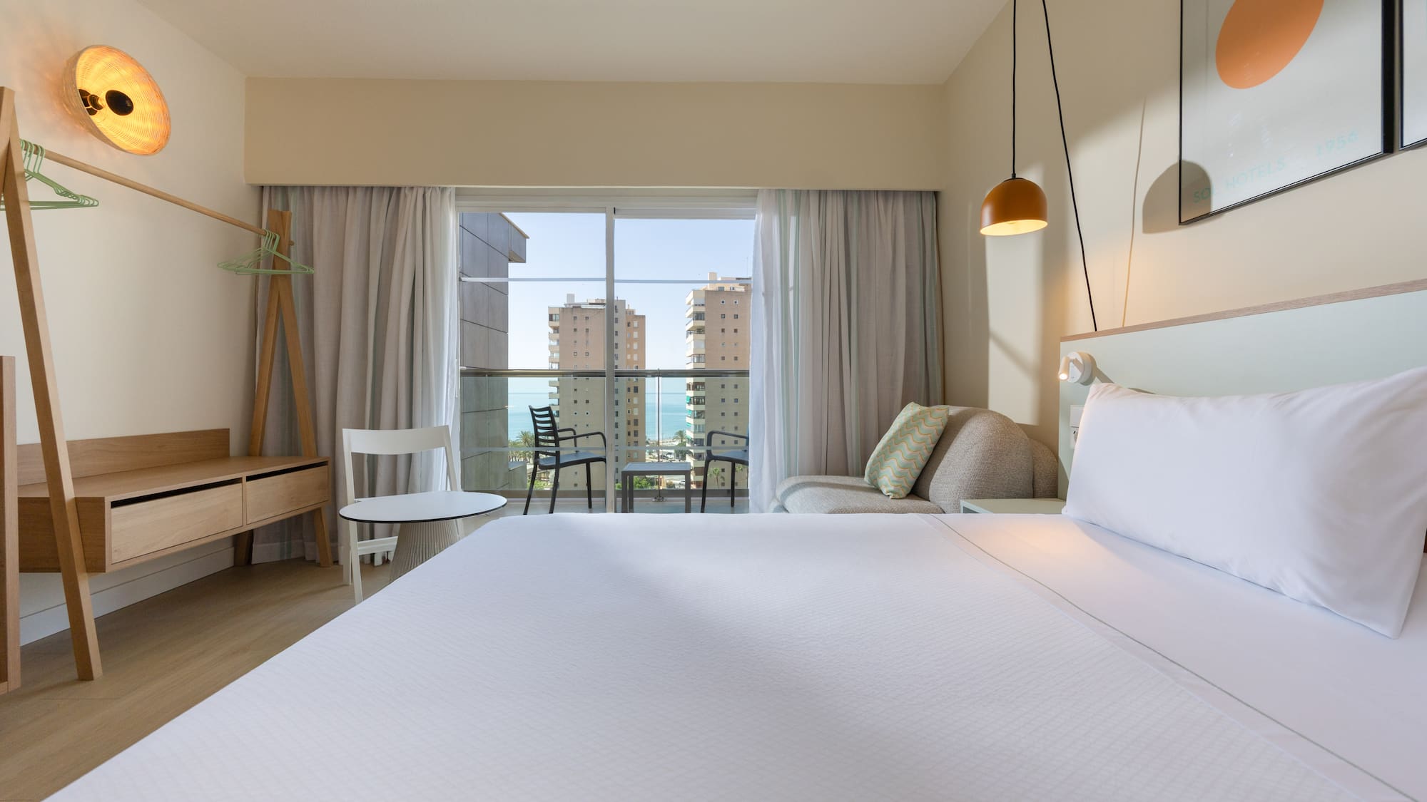 Modern hotel room with ocean view balcony, large bed, and contemporary decor.
