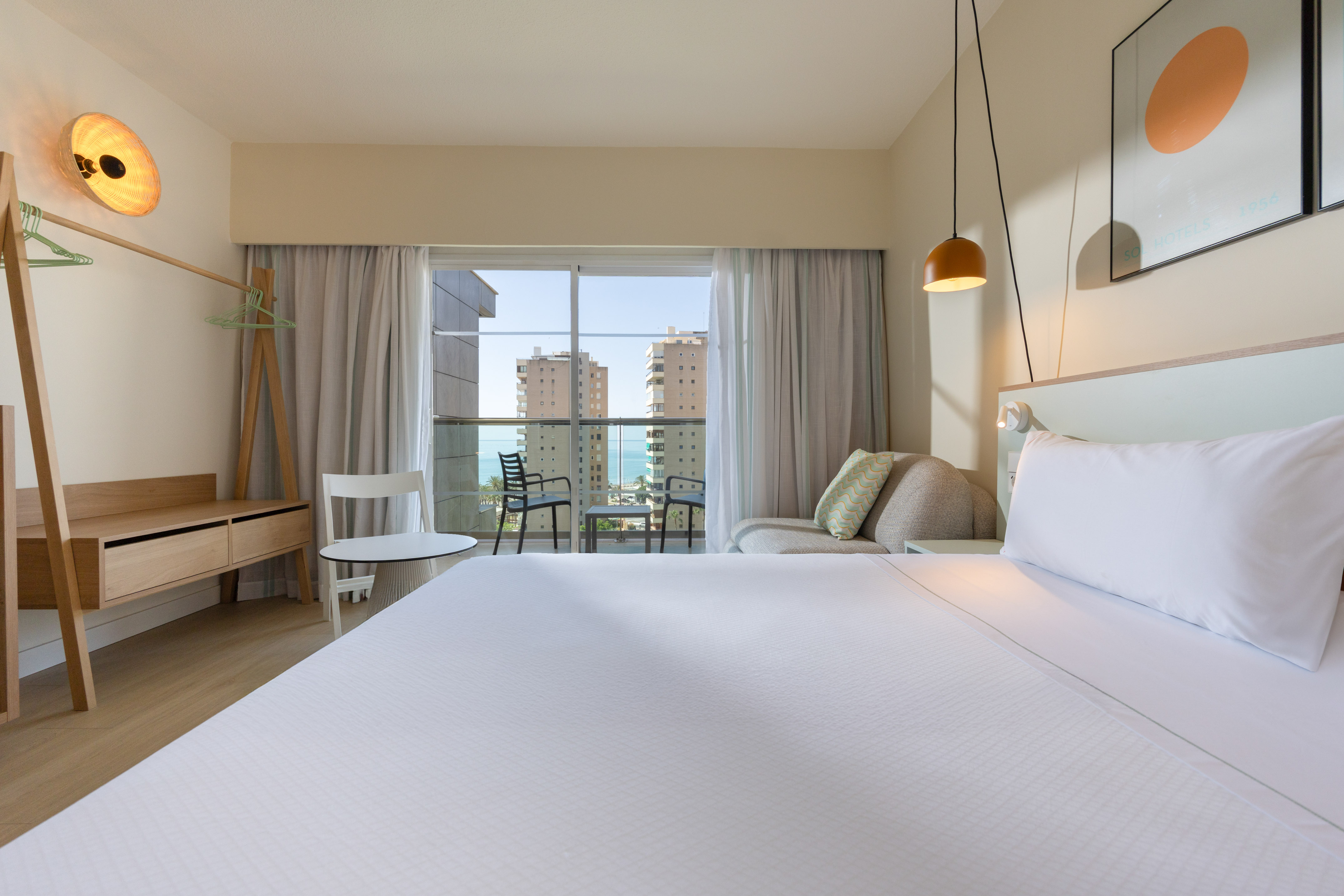 Hotel room with ocean view balcony, white bed, and modern decor.