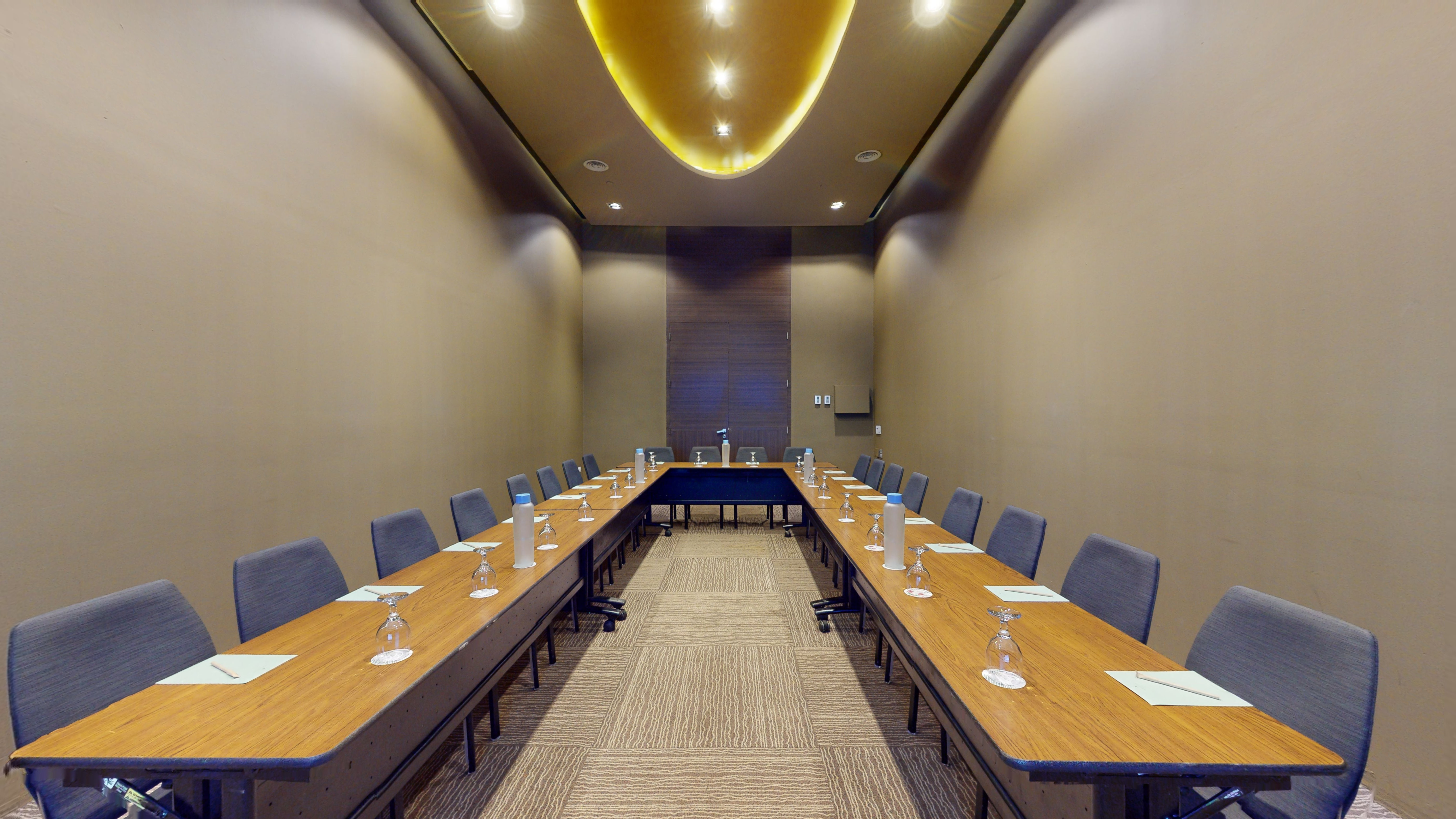 U-shaped conference room, wood tables, gray chairs, illuminated ceiling.
