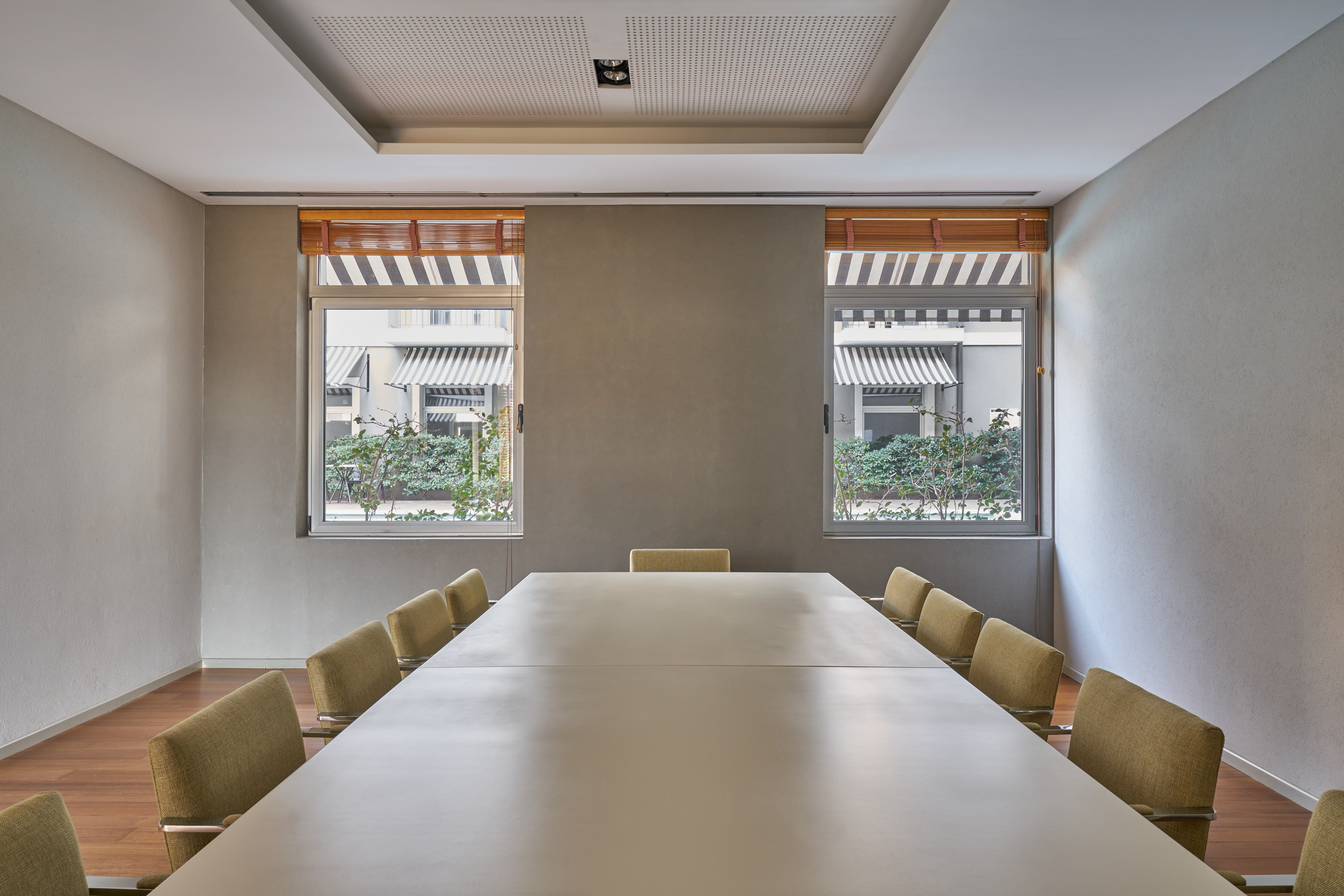 Modern conference room with long table, olive chairs, wood floor, and two windows.