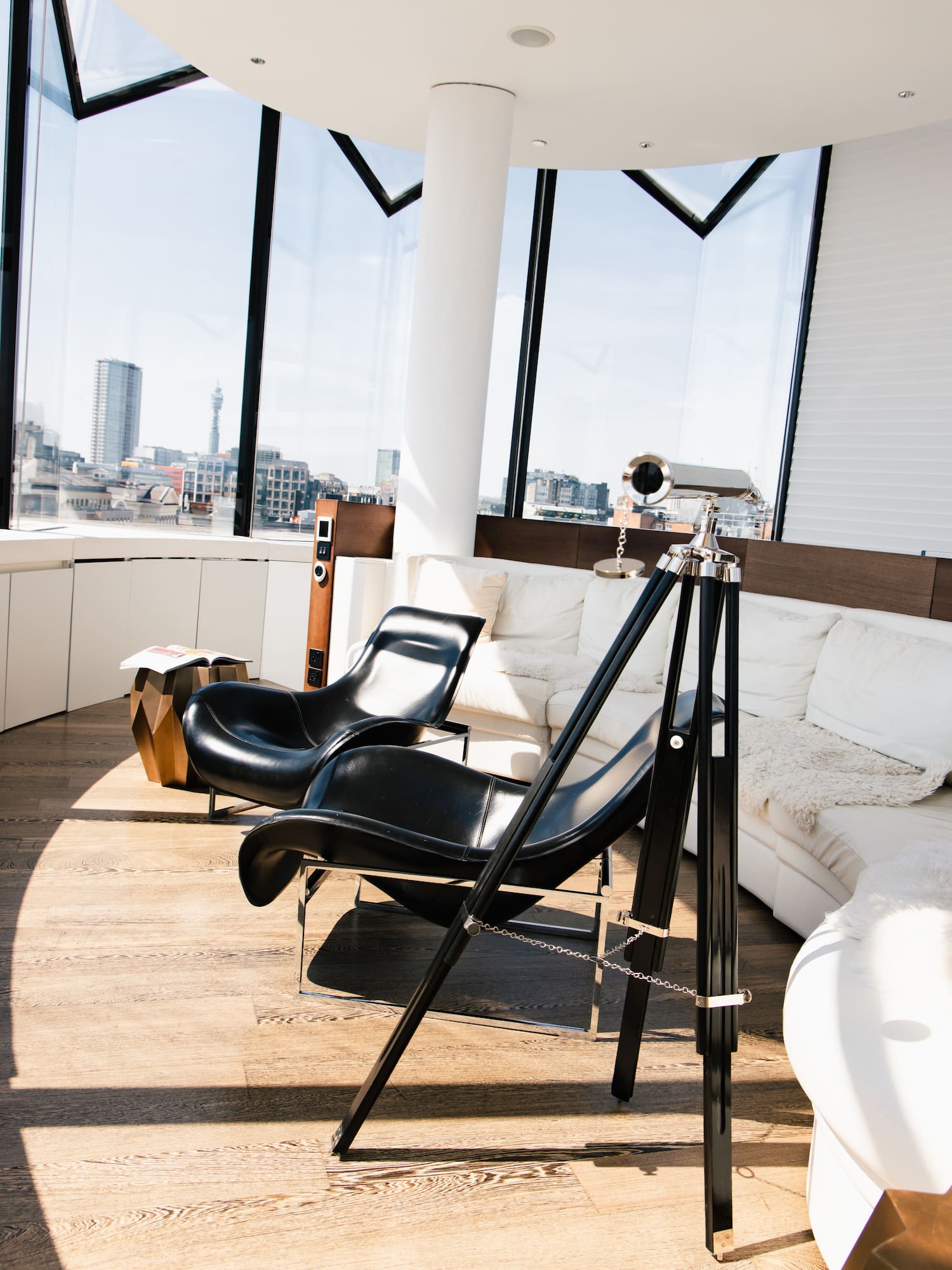 Modern living room with city view, black leather chairs, white sofa, telescope.