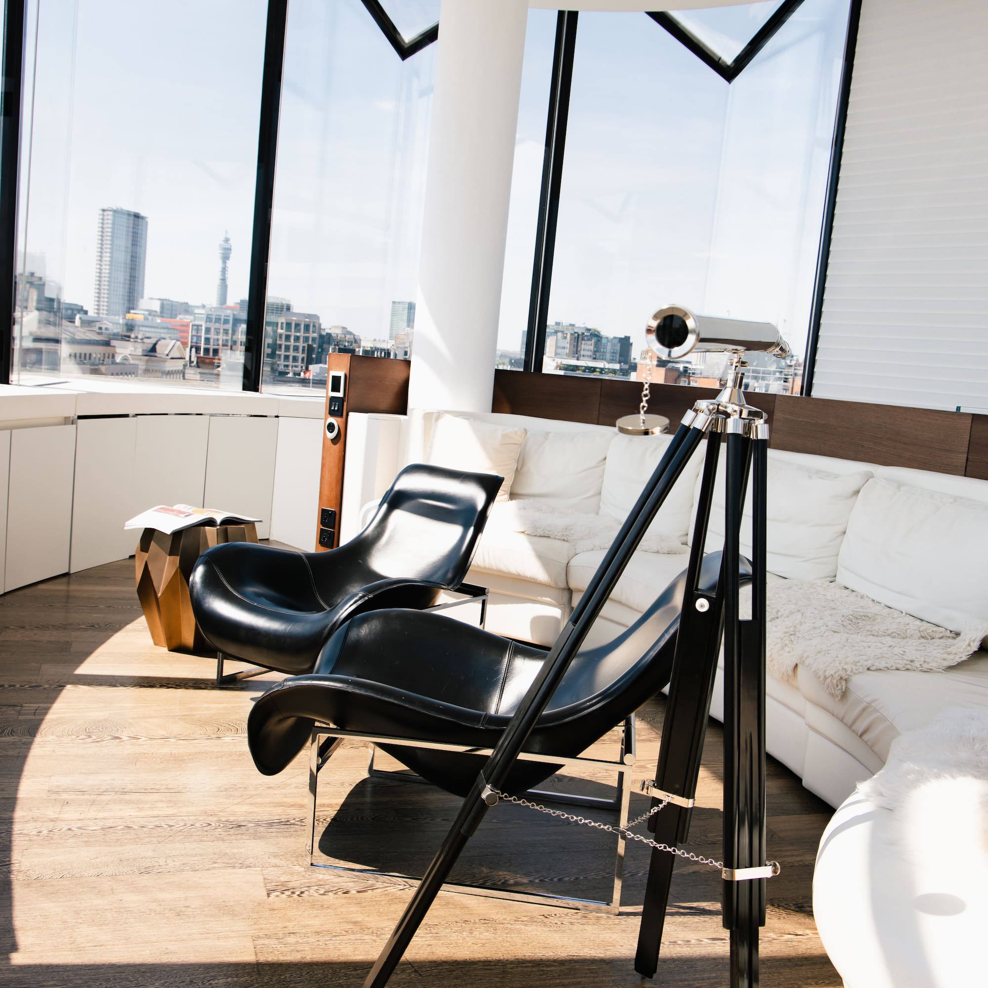 Modern living room with city view, black leather chairs, white sofa, telescope.