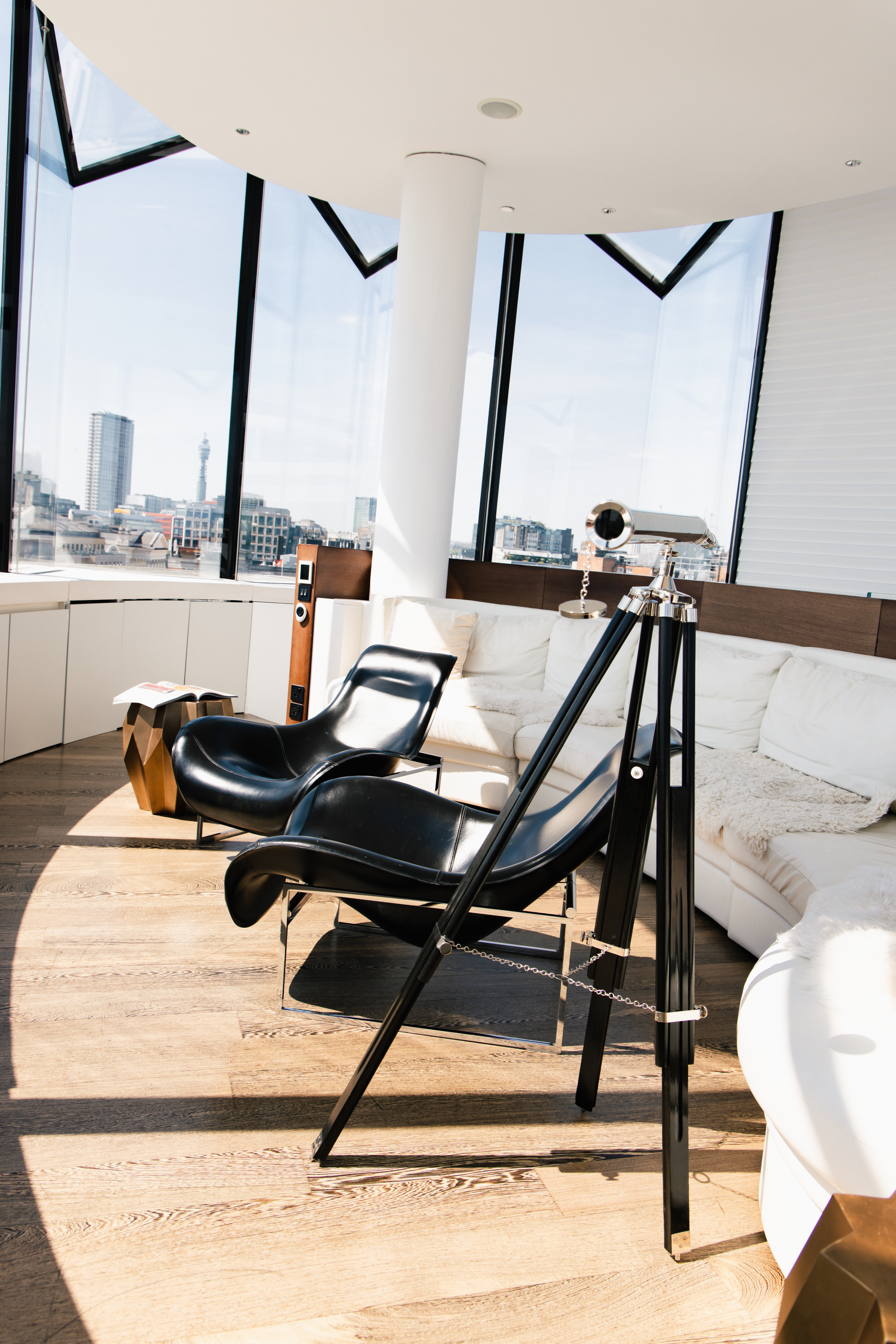 Modern living room with city view, black leather chairs, white sofa, telescope.