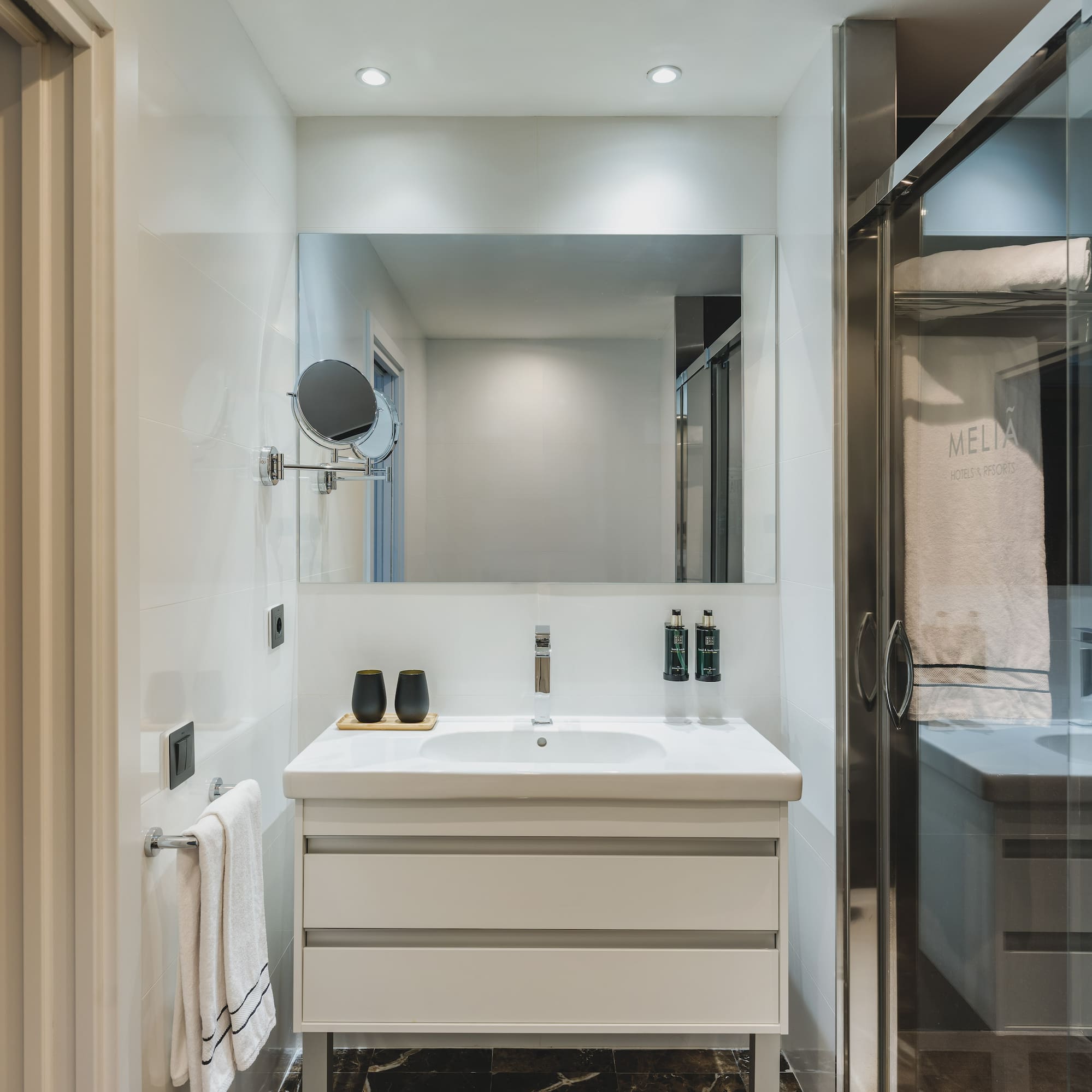 Baño moderno de hotel Meliá con lavabo, espejo y ducha acristalada.