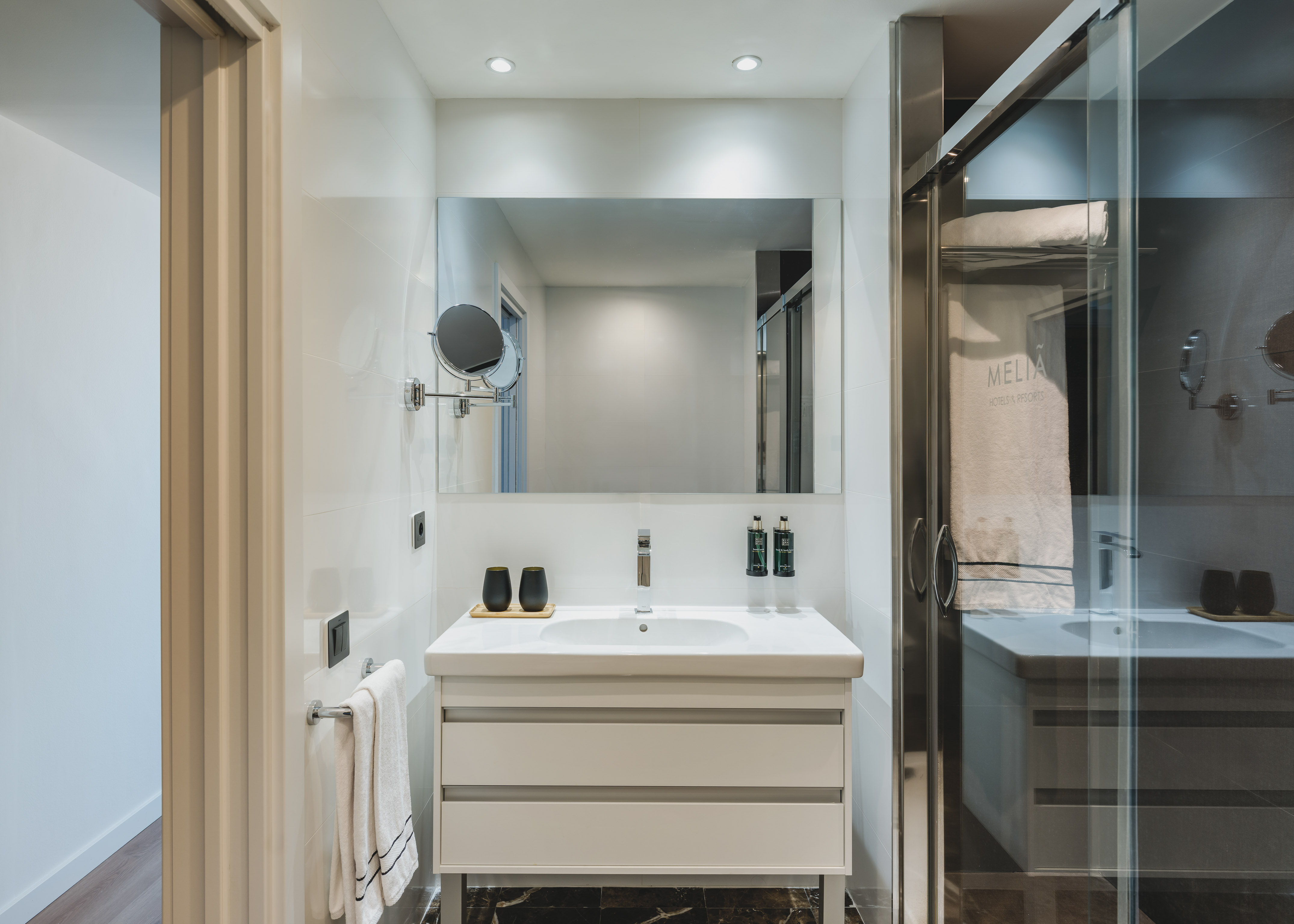 Baño moderno de hotel Meliá con lavabo, espejo y ducha acristalada.