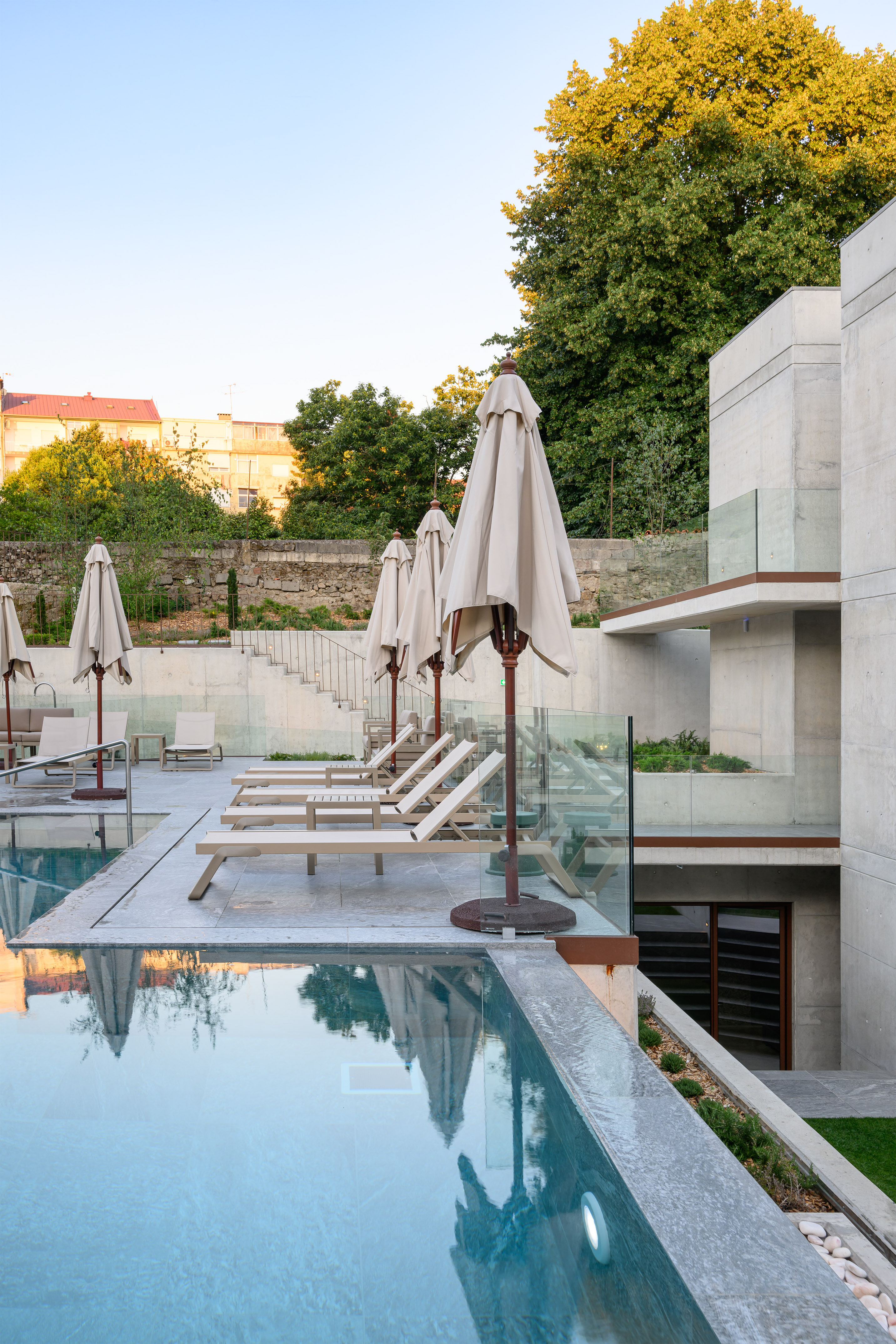 Modern concrete pool area with sun loungers and closed parasols.