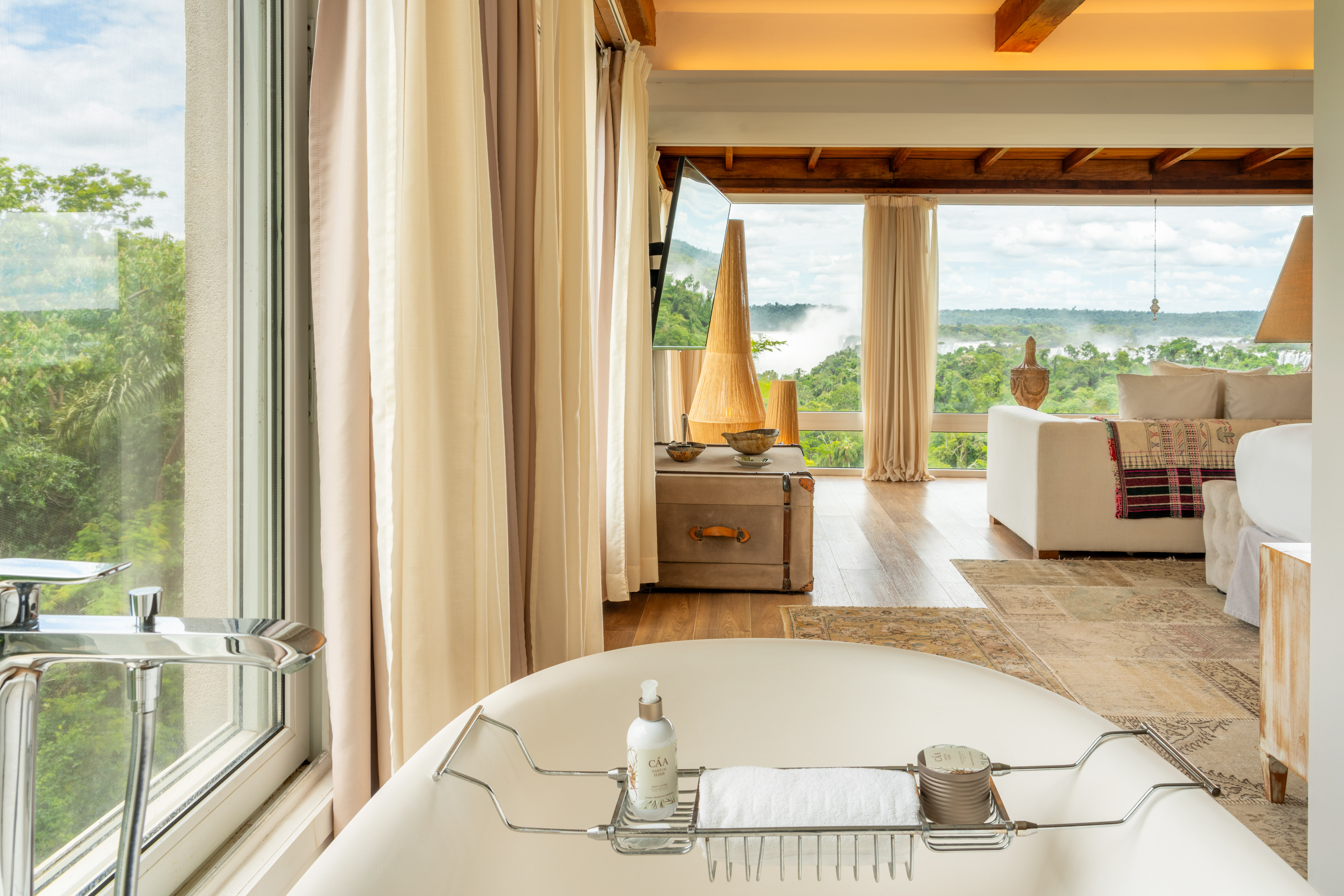Freestanding bathtub in luxury suite with panoramic jungle and waterfall views.