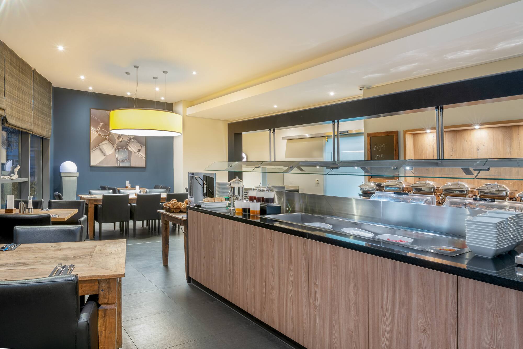 Modern hotel dining room with breakfast buffet line and seating.