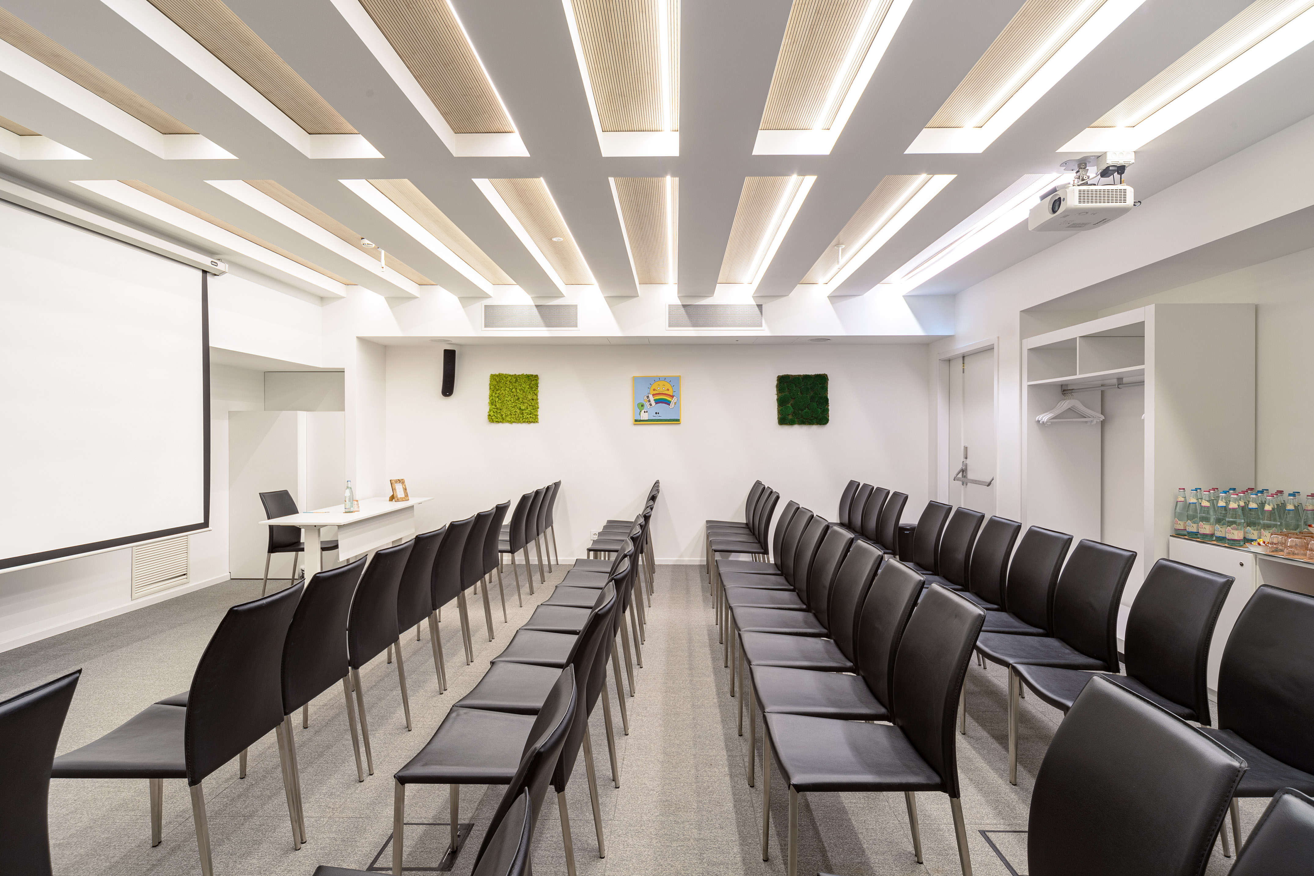 Modern conference room with projector screen, black chairs, and ceiling lighting.