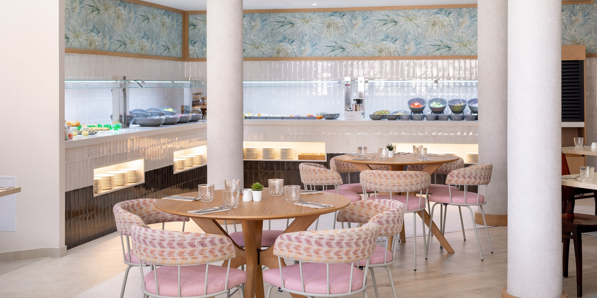 Modern hotel buffet restaurant with pink chairs and wooden tables.