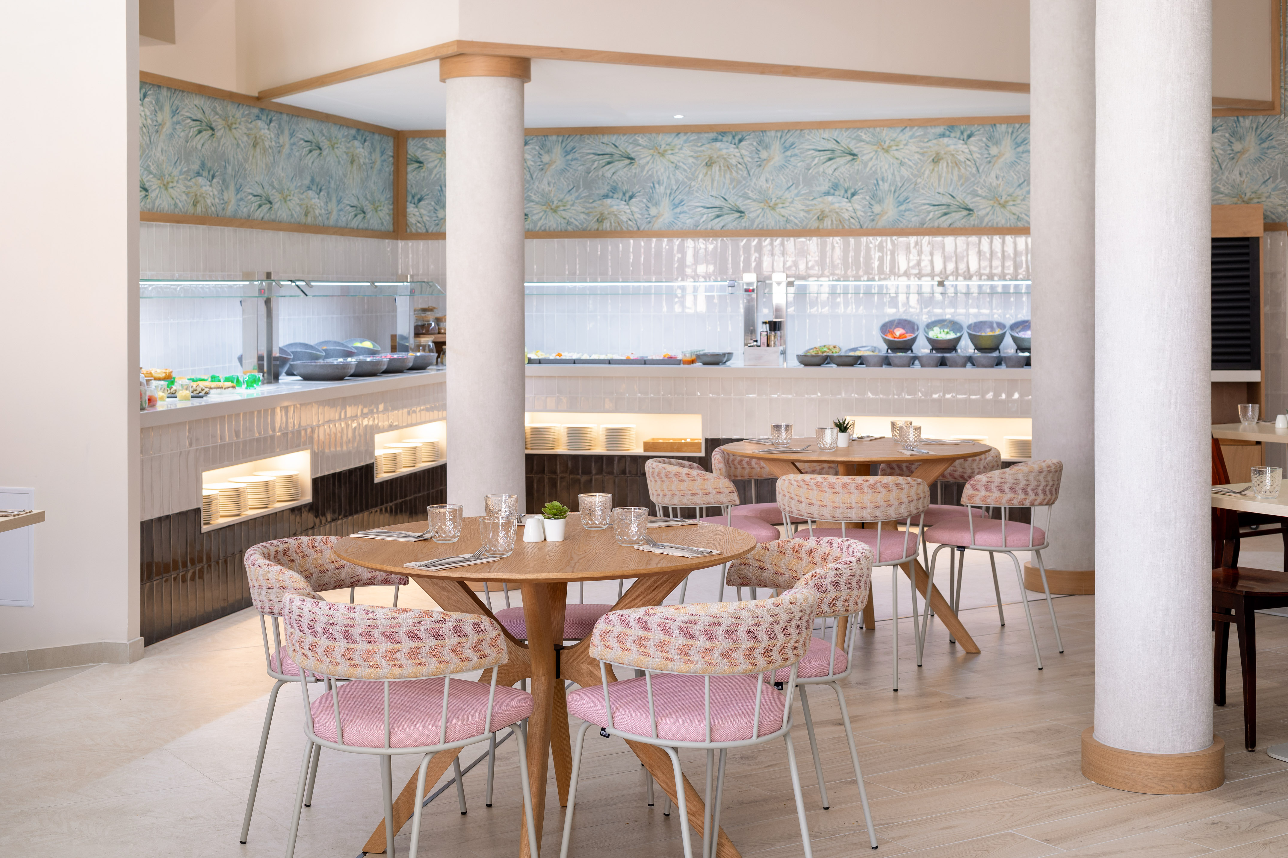 Modern hotel buffet restaurant with pink chairs and wooden tables.