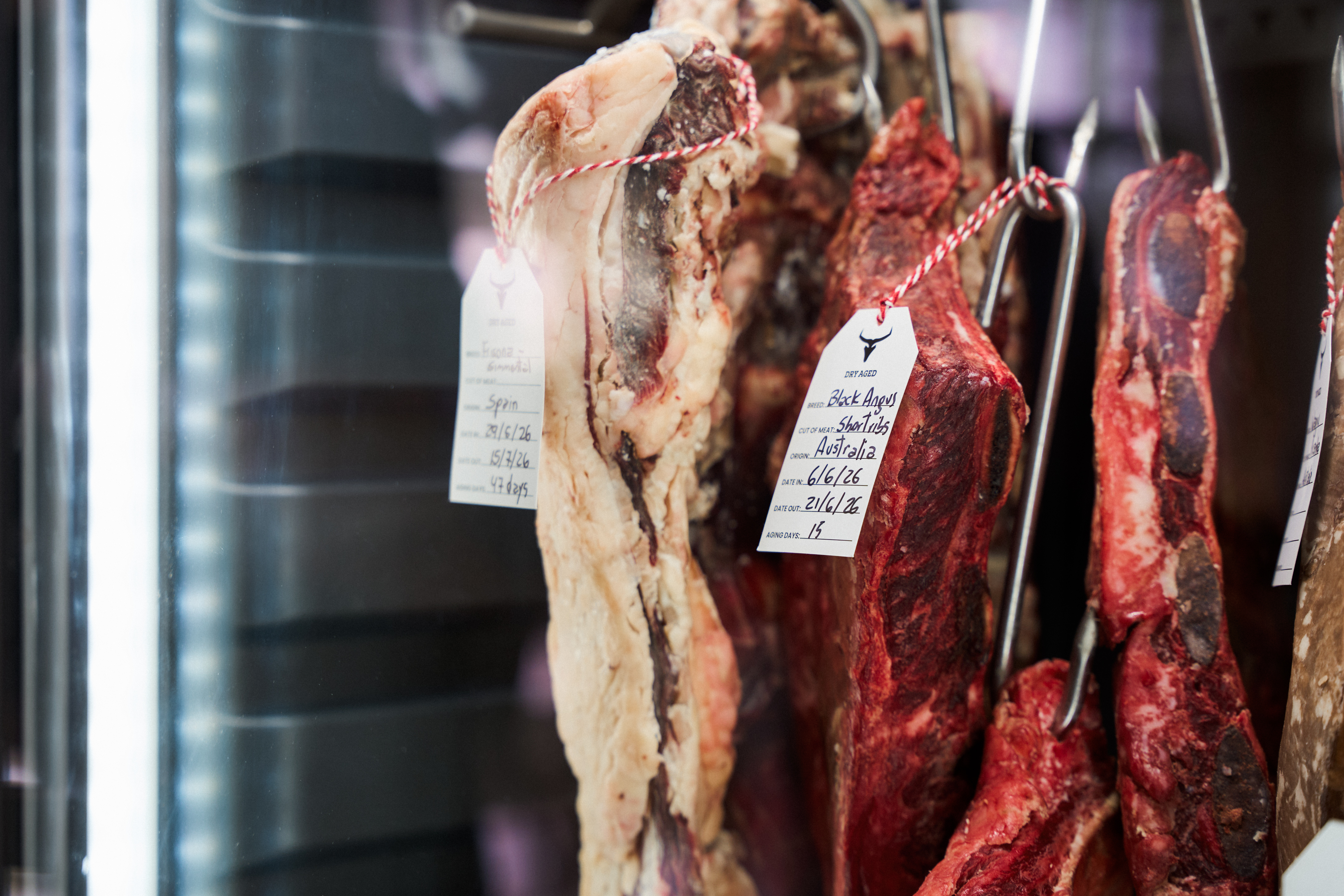 Dry-aged Black Angus short ribs and premium beef hanging in a butcher display.