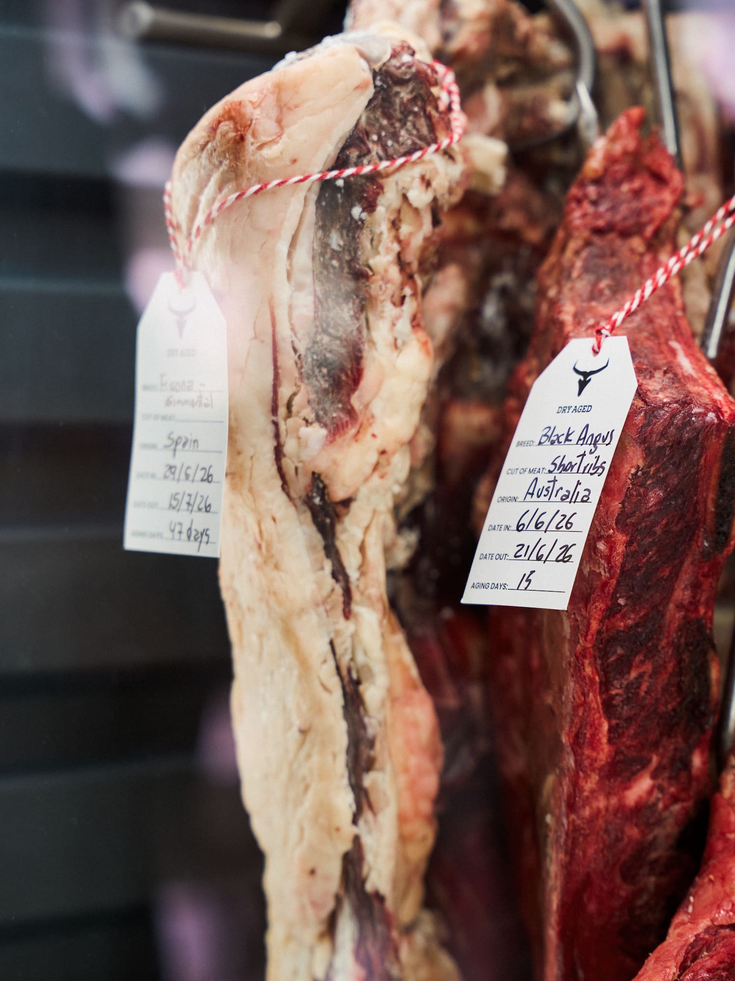 Dry-aged Black Angus short ribs and premium beef hanging in a butcher display.
