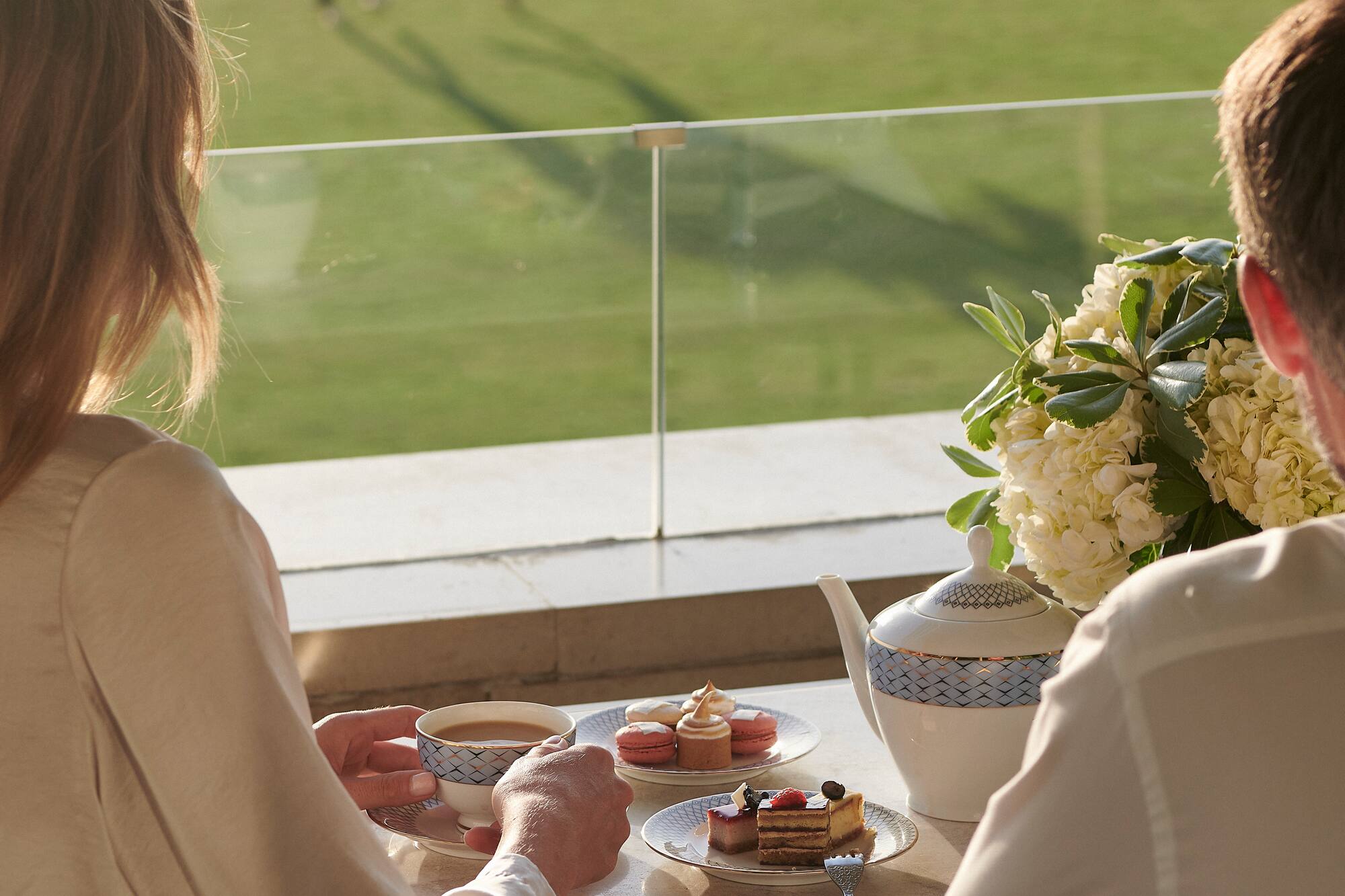 Couple enjoying afternoon tea and desserts on a balcony, watching a polo match.