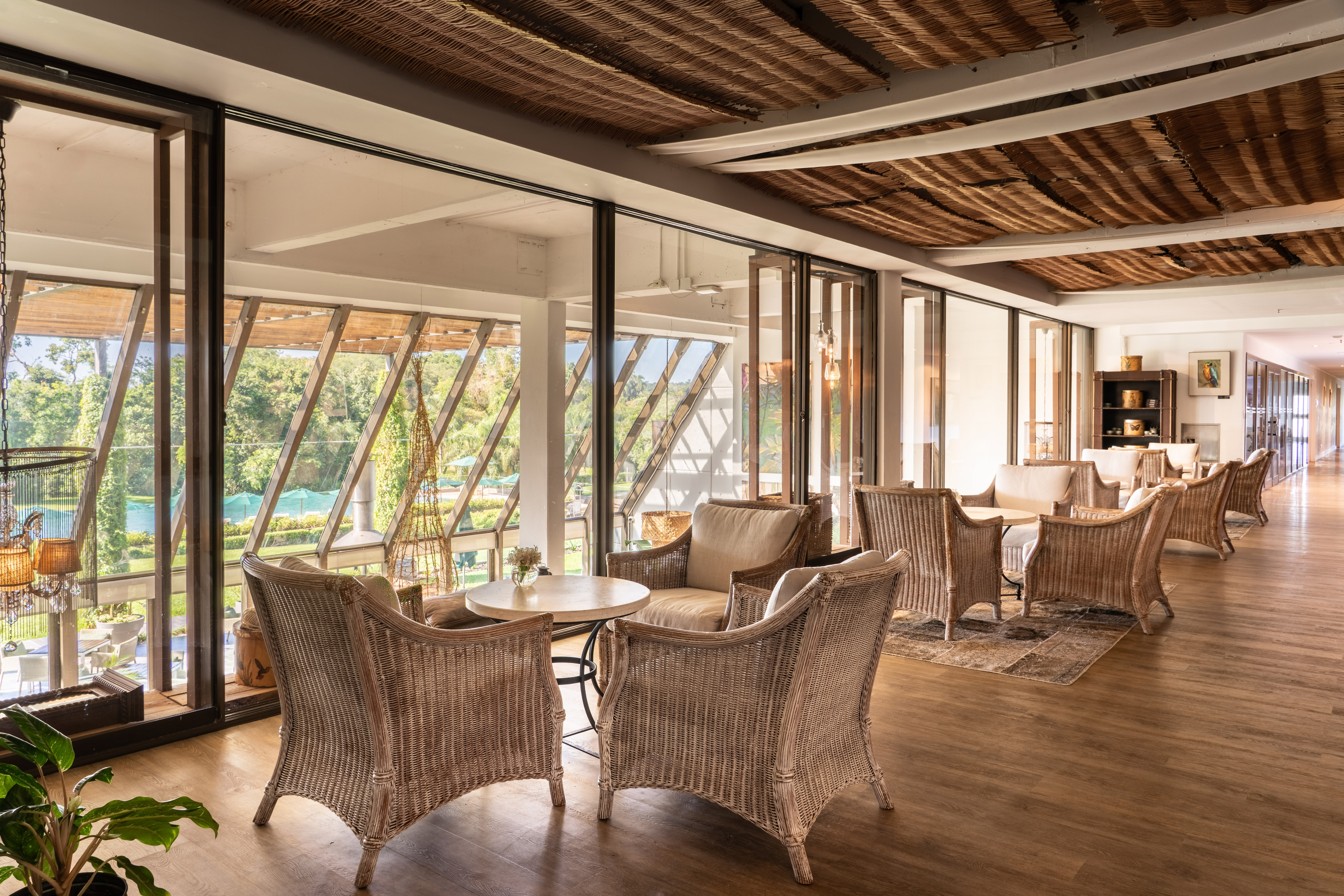 Hotel lounge with wicker furniture, woven ceiling, large windows overlooking a lush garden.