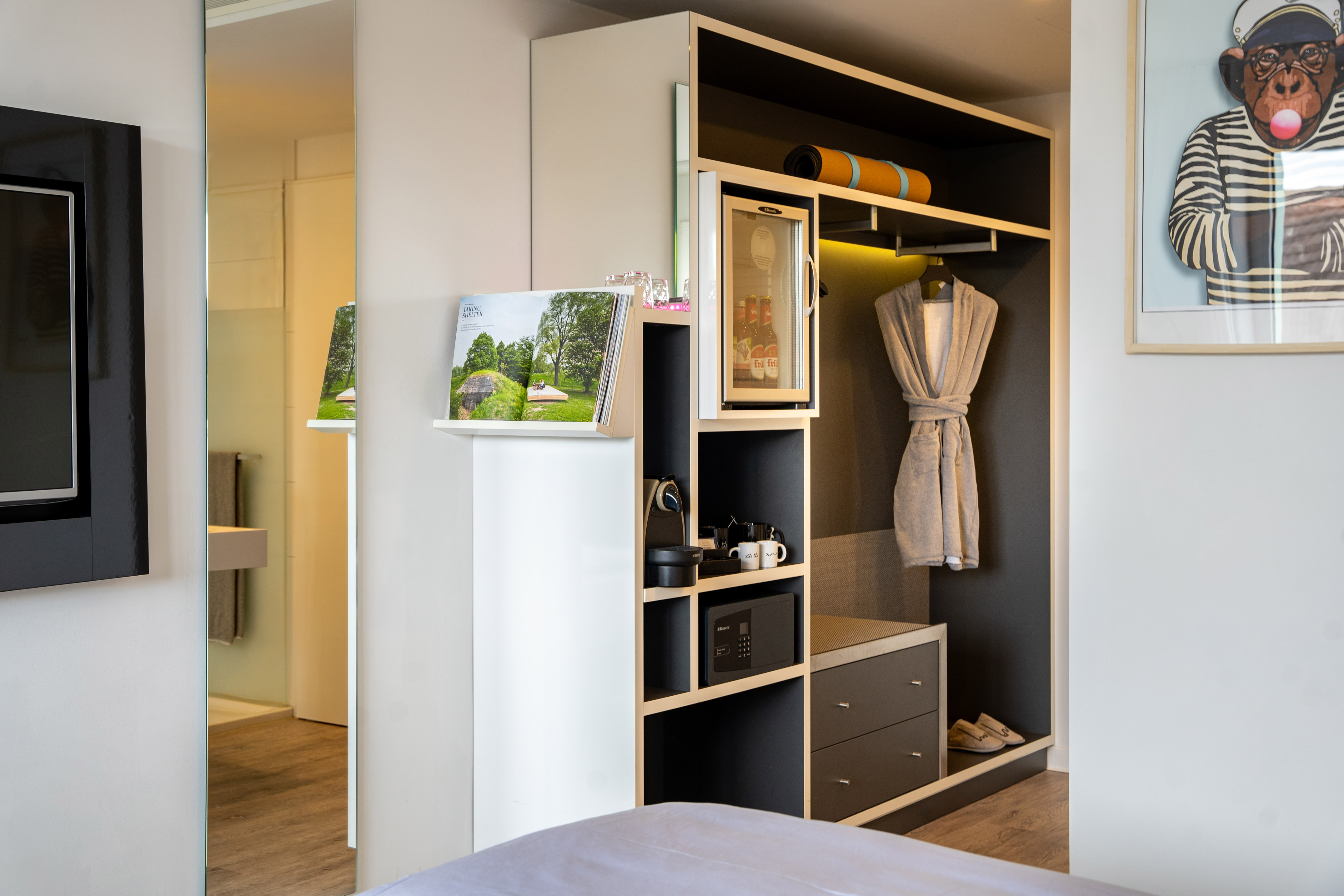 Modern hotel room with built-in wardrobe, mini-bar, coffee machine, and bathrobe.