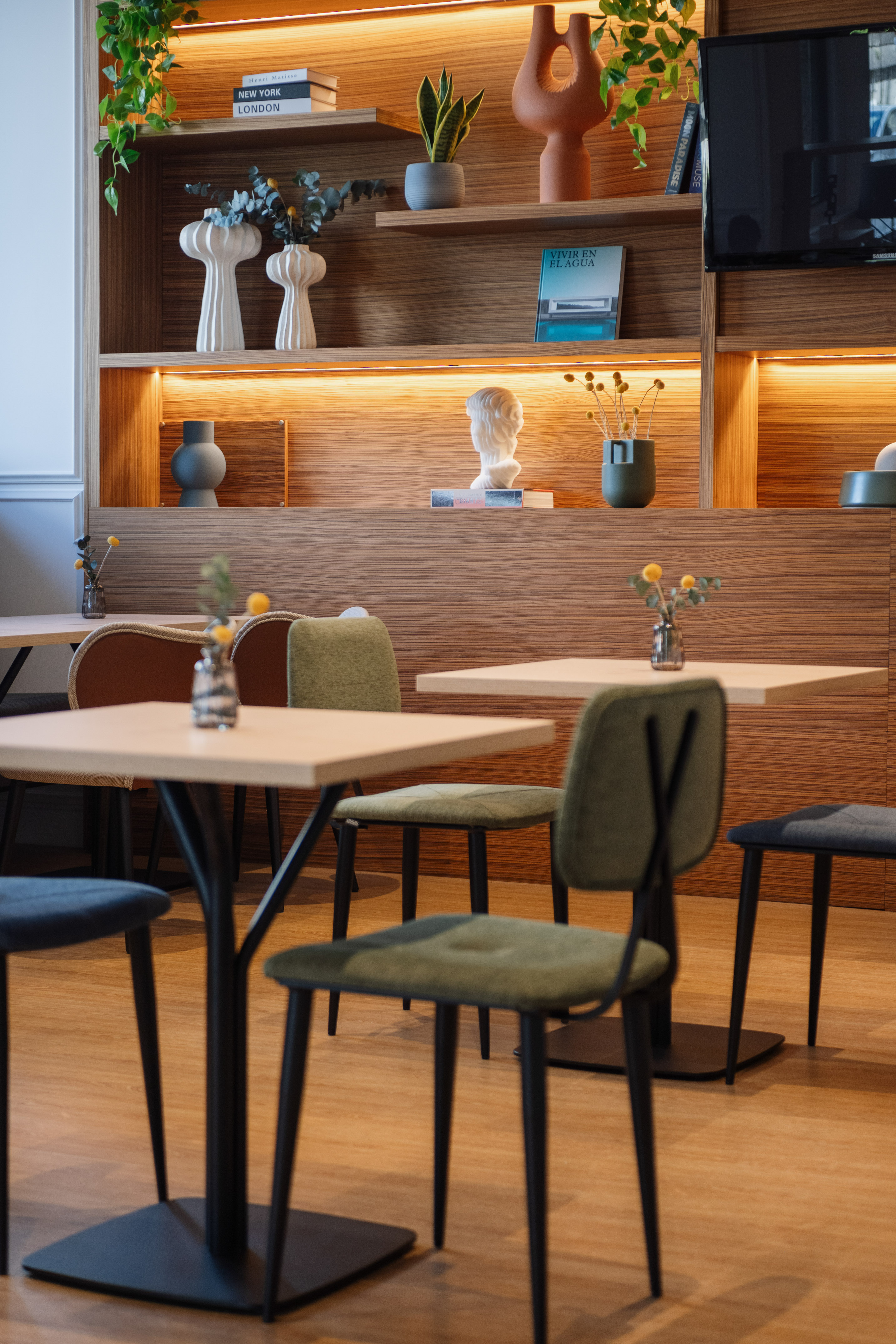 Modern cafe interior with backlit wooden shelves, diverse decor, and dining tables.