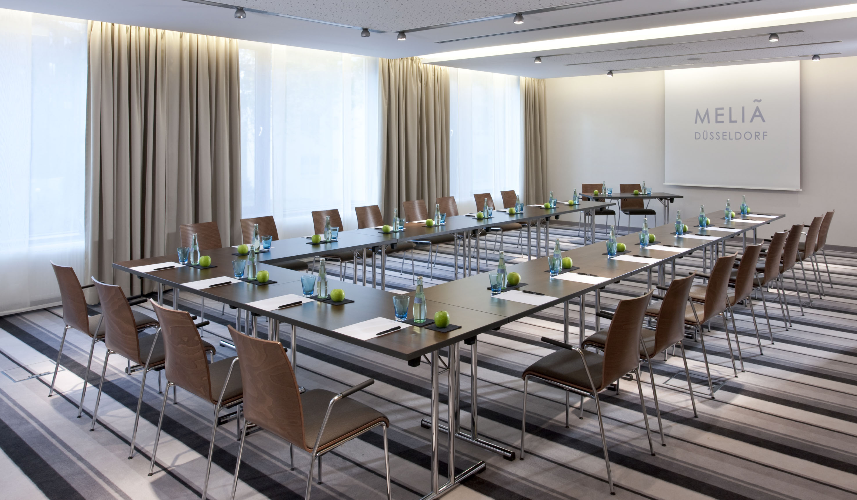 Meliá Düsseldorf conference room, U-shape setup with tables, chairs, screen.