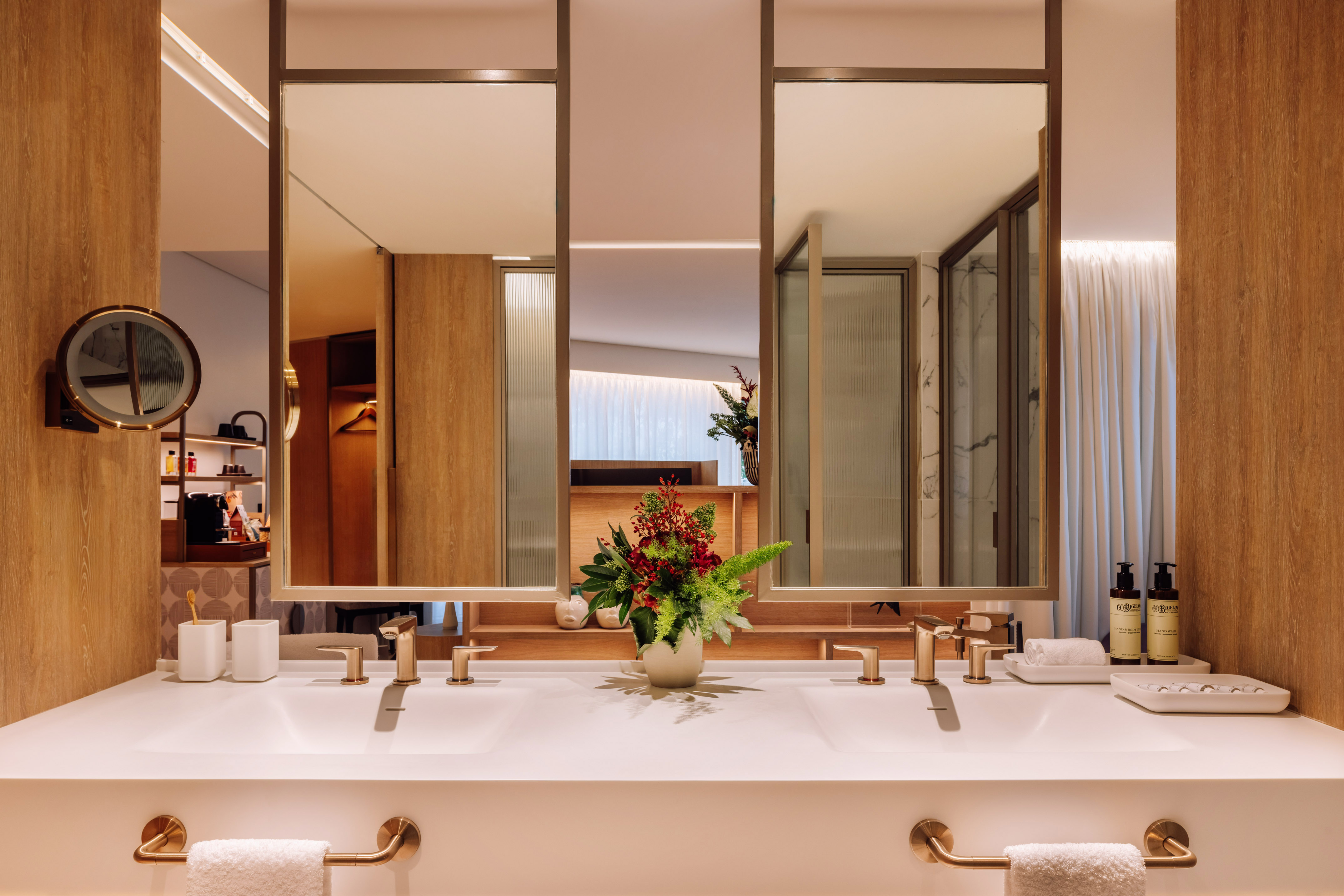 Modern double vanity hotel bathroom with gold fixtures and wooden details.