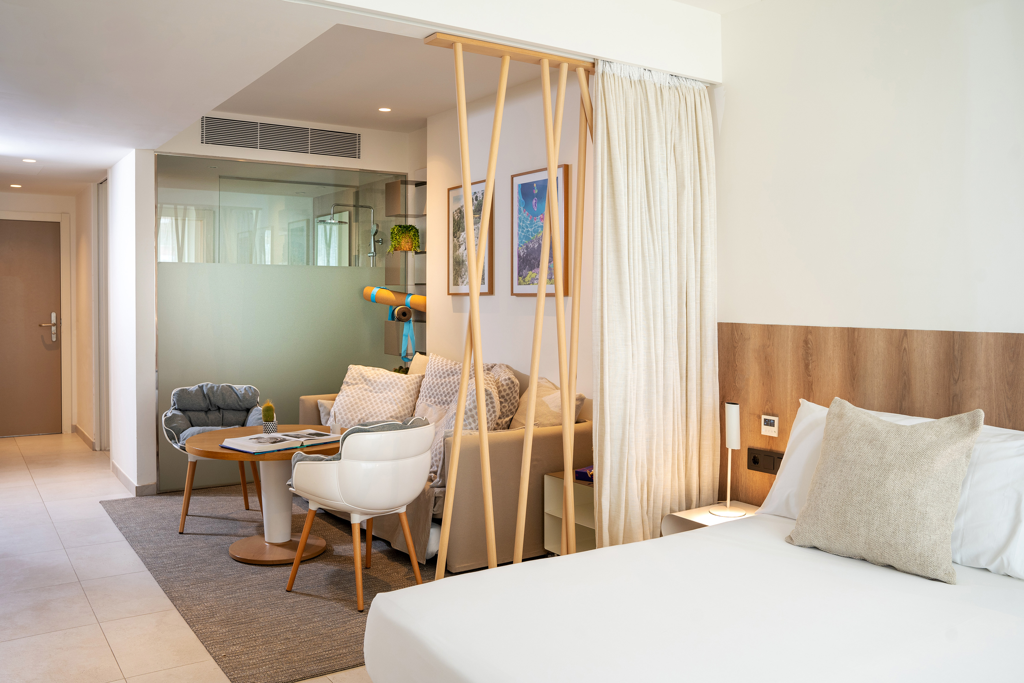 Bright modern hotel suite with bed, sofa, living area, and glass shower.