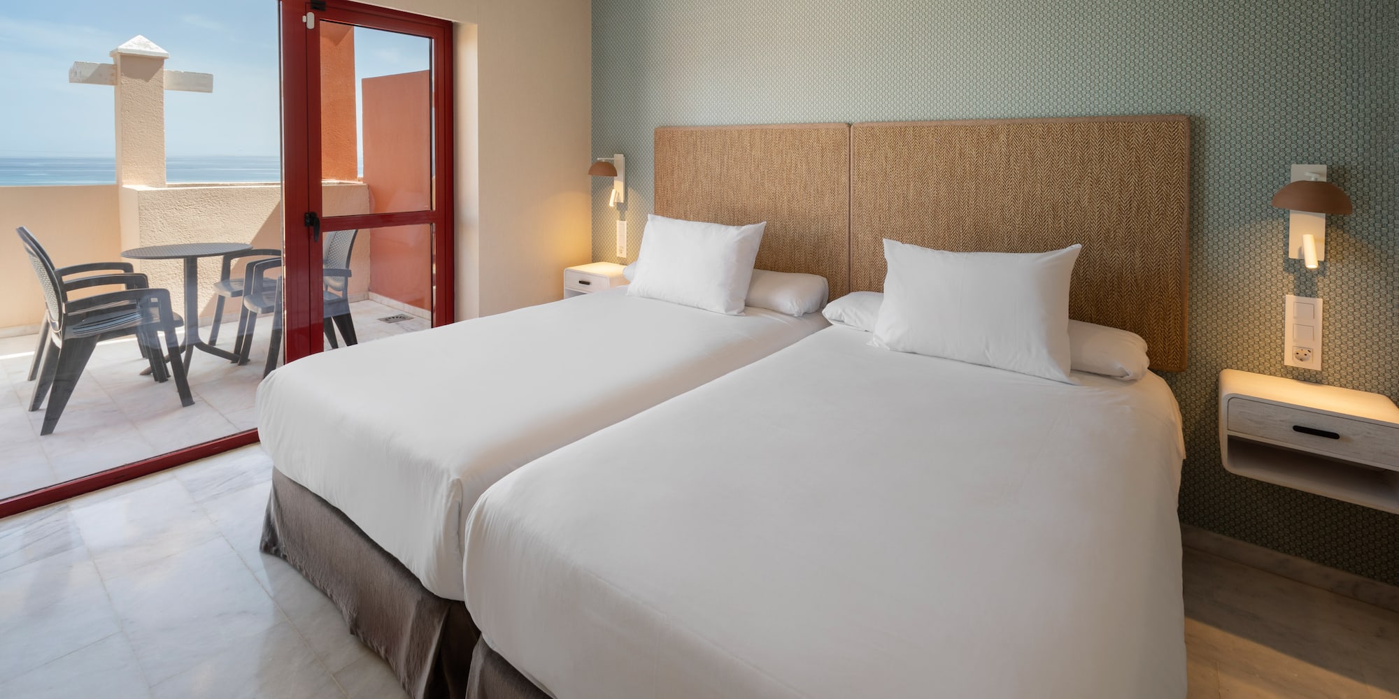 Hotel room with twin beds, balcony, and ocean view.