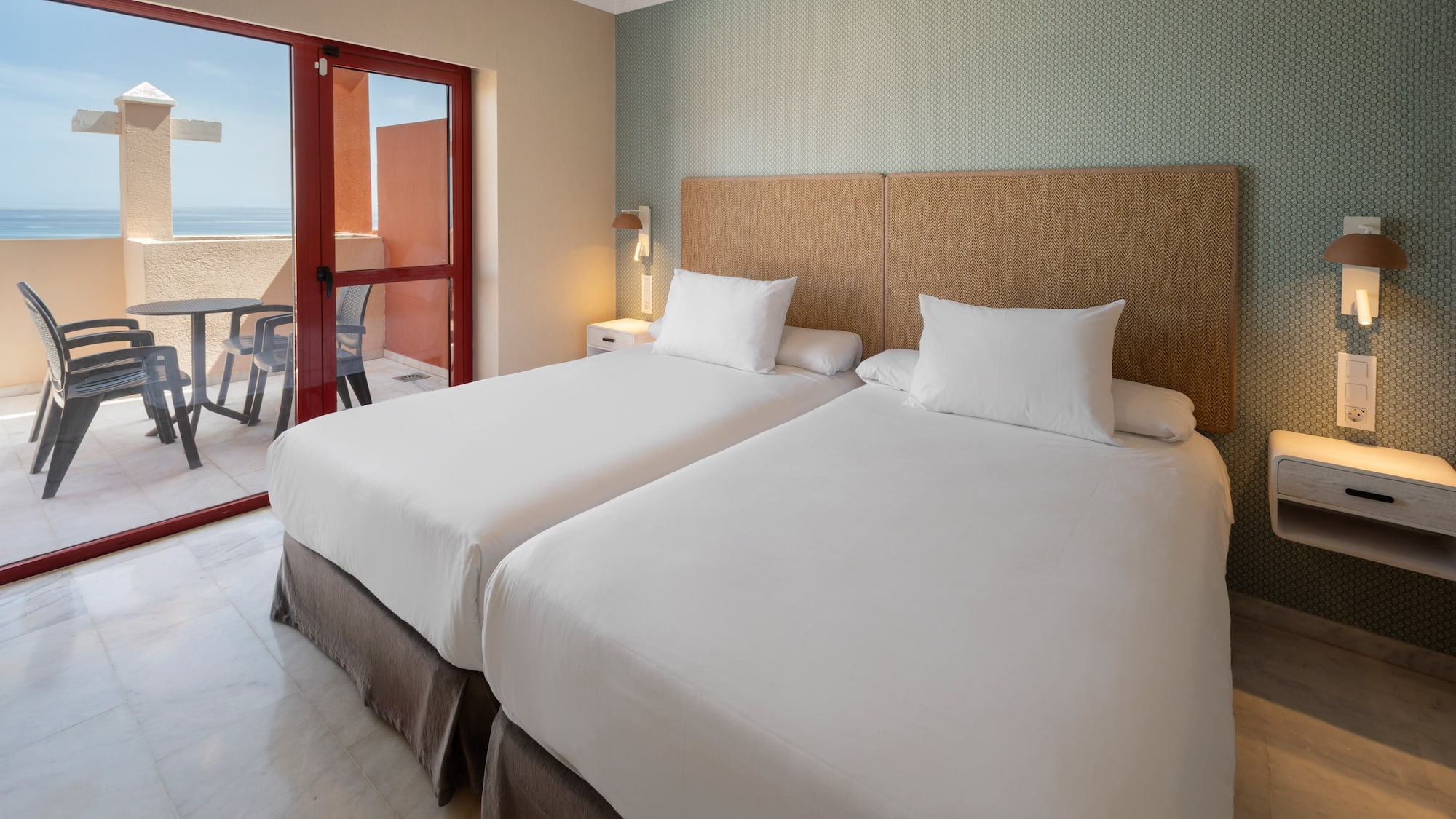 Hotel room with twin beds, balcony, and ocean view.