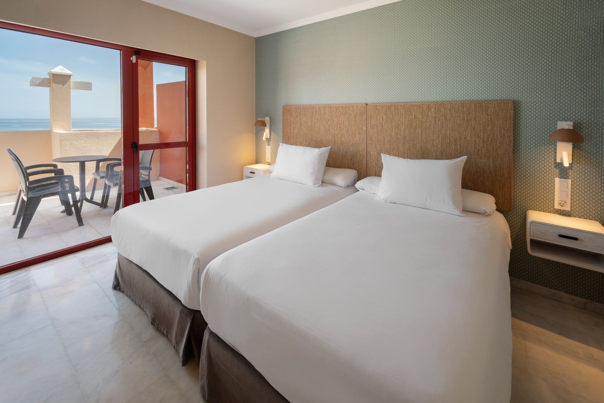 Hotel room with twin beds, balcony, and ocean view.