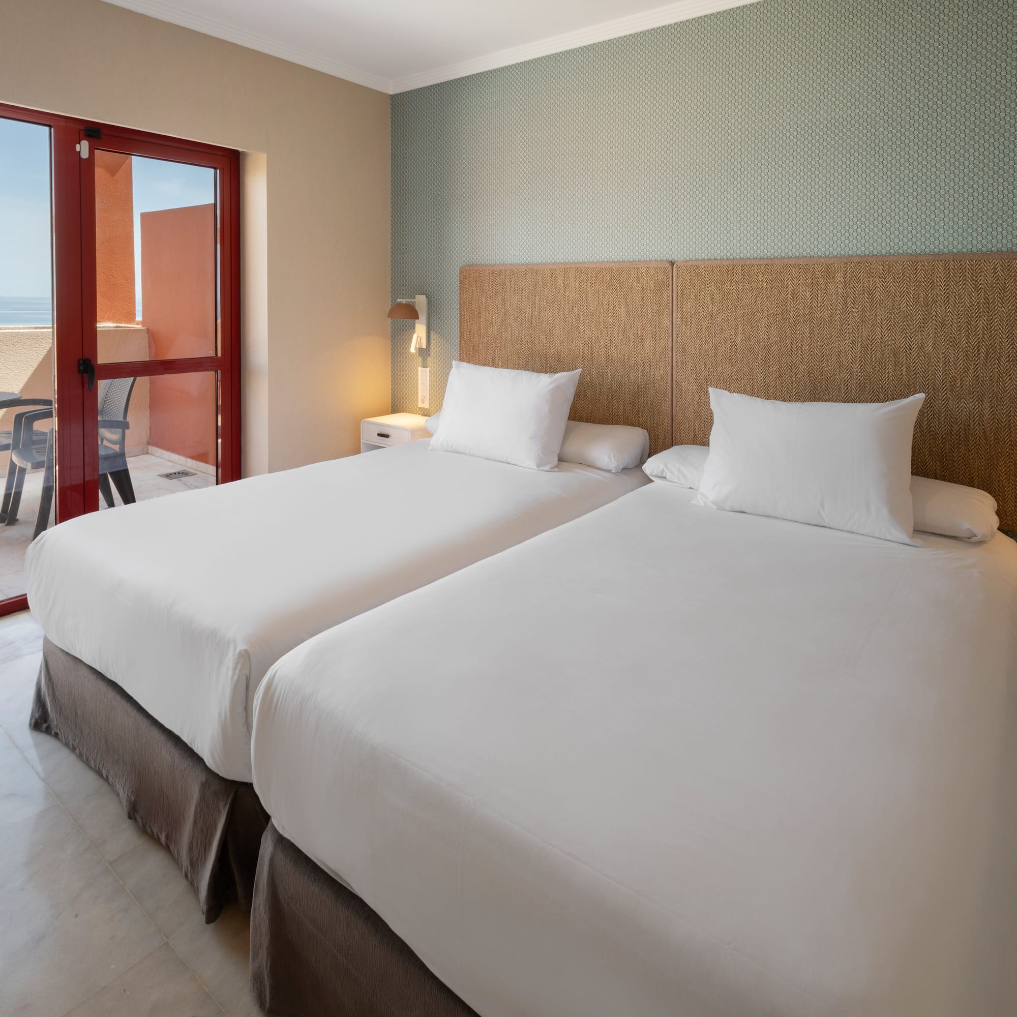 Hotel room with twin beds, balcony, and ocean view.