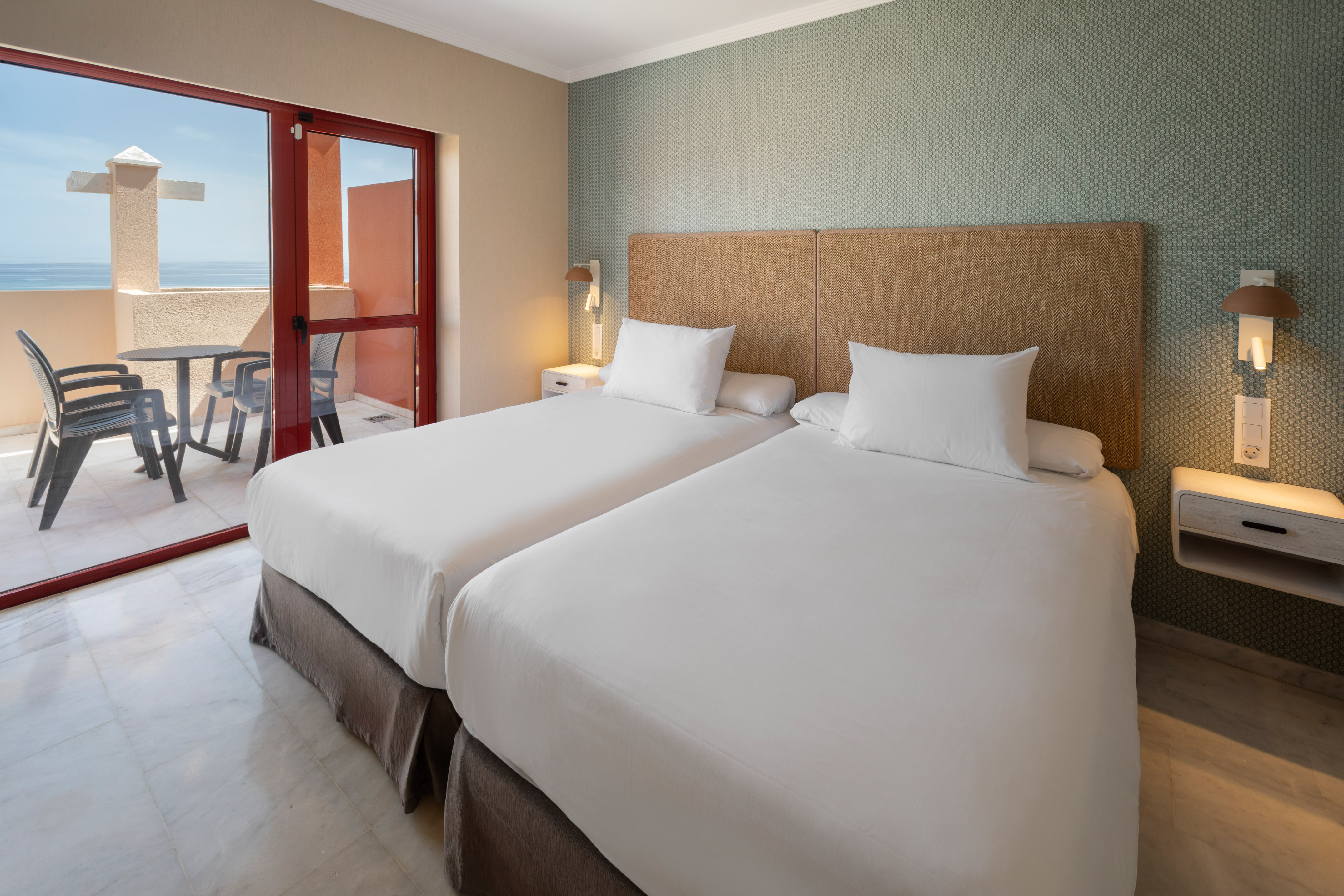 Hotel room with twin beds, balcony, and ocean view.