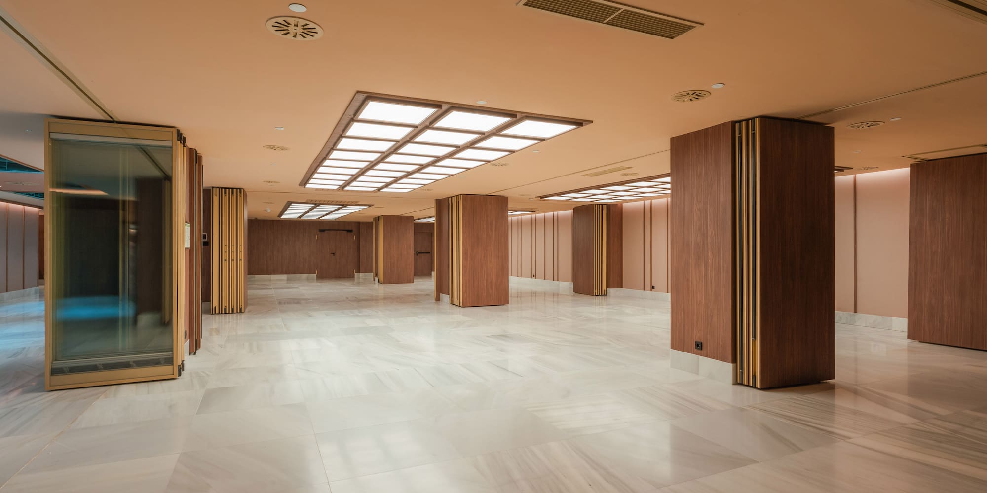 Modern lobby with marble floor, wooden columns, and bright recessed lighting.