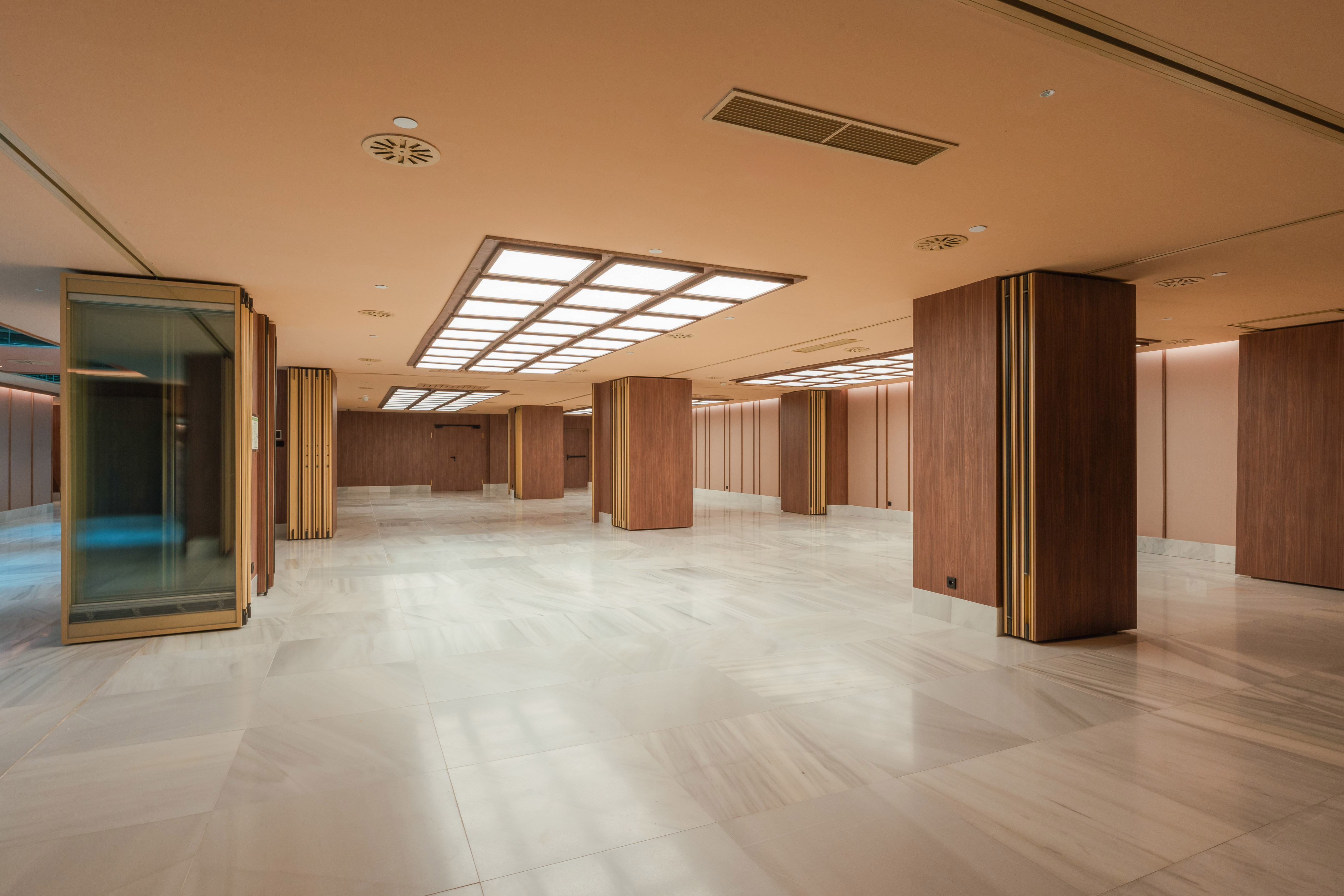 Modern lobby with marble floor, wooden columns, and bright recessed lighting.