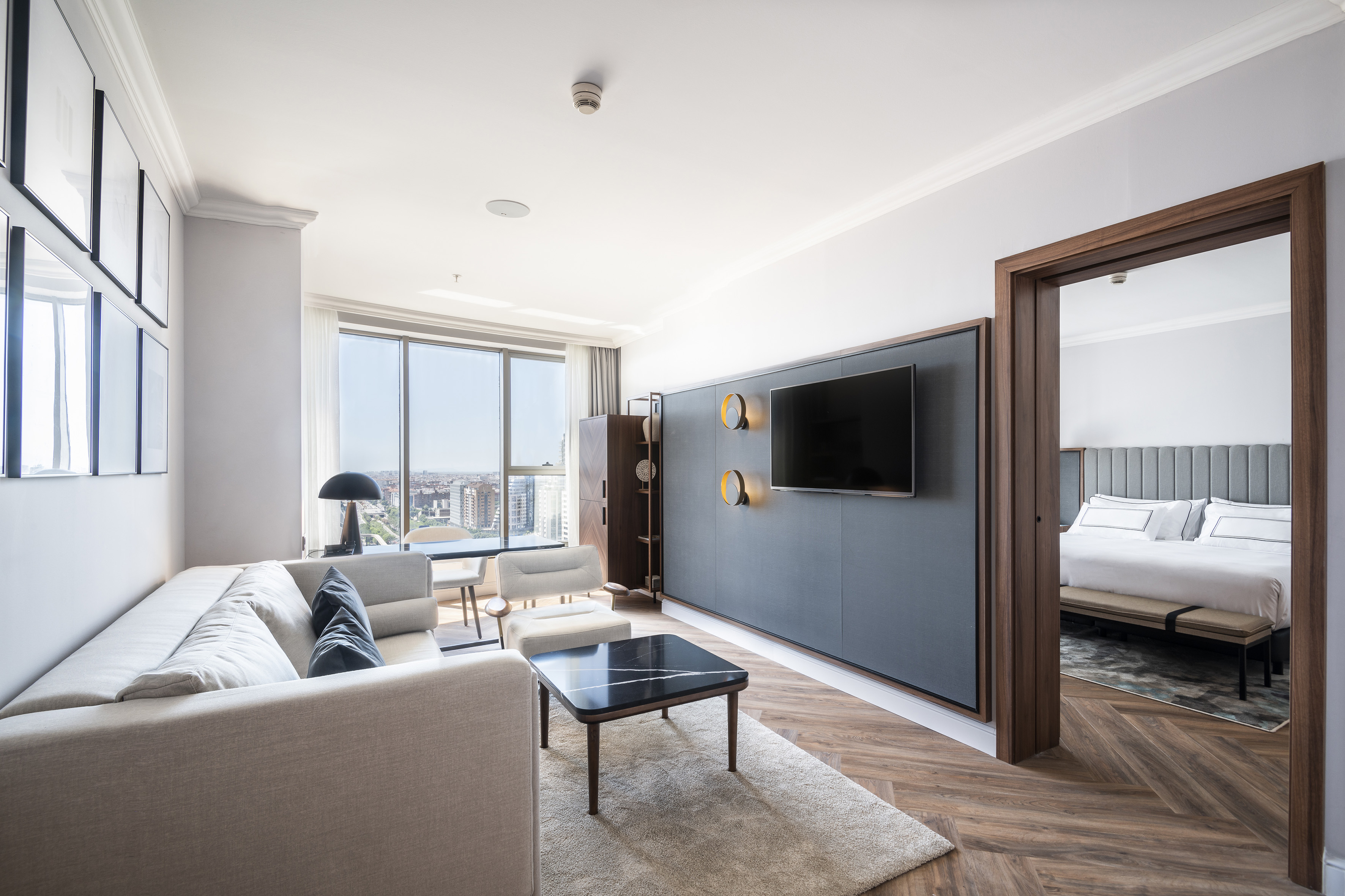 Moderna suite de hotel con sala, sofá, TV, dormitorio y vistas urbanas.