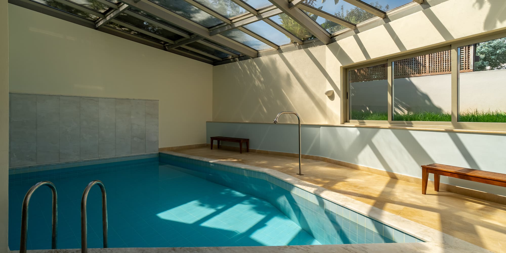Modern indoor pool with glass skylight roof and blue tiles.