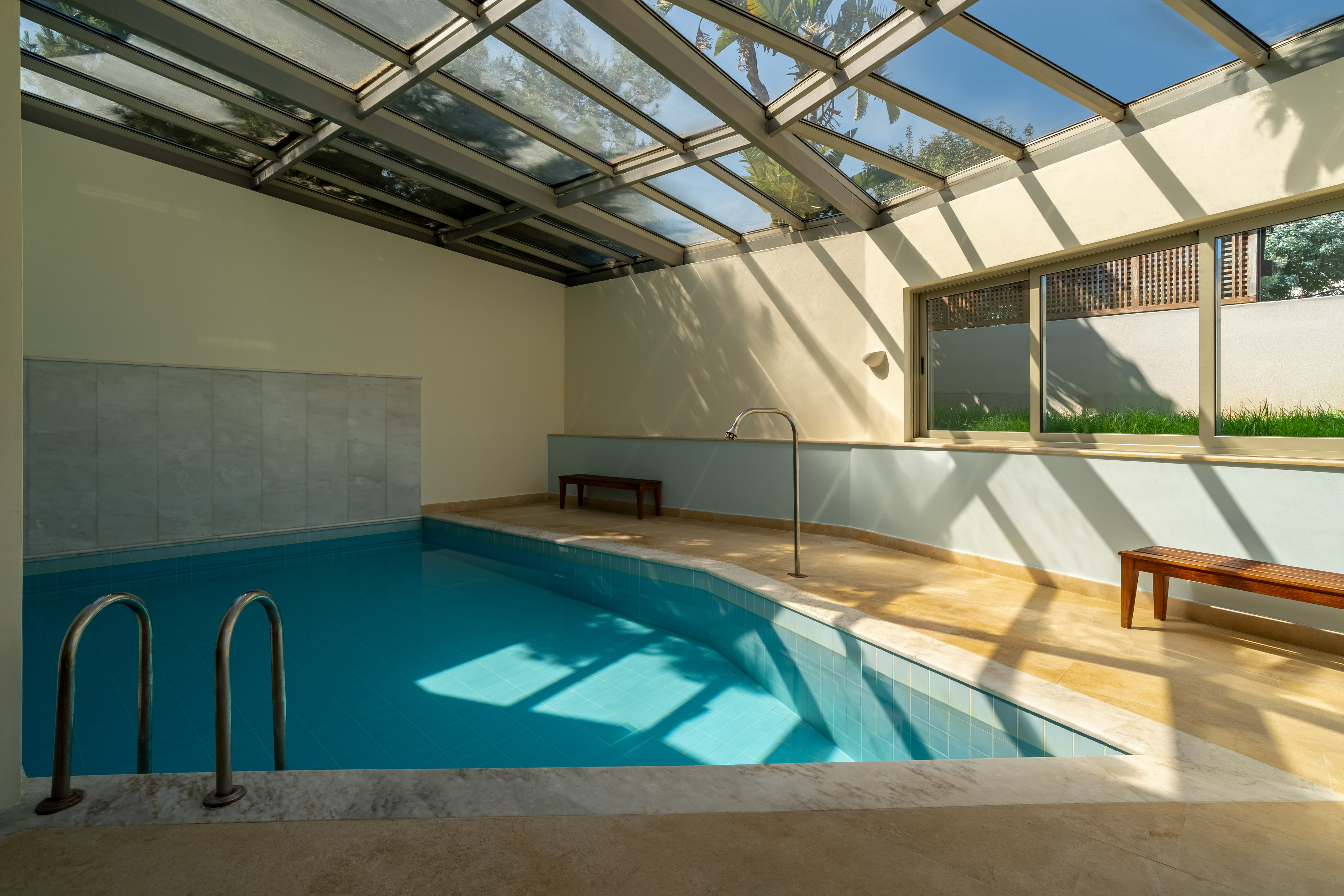 Indoor swimming pool under glass roof, blue tiled water, natural light.