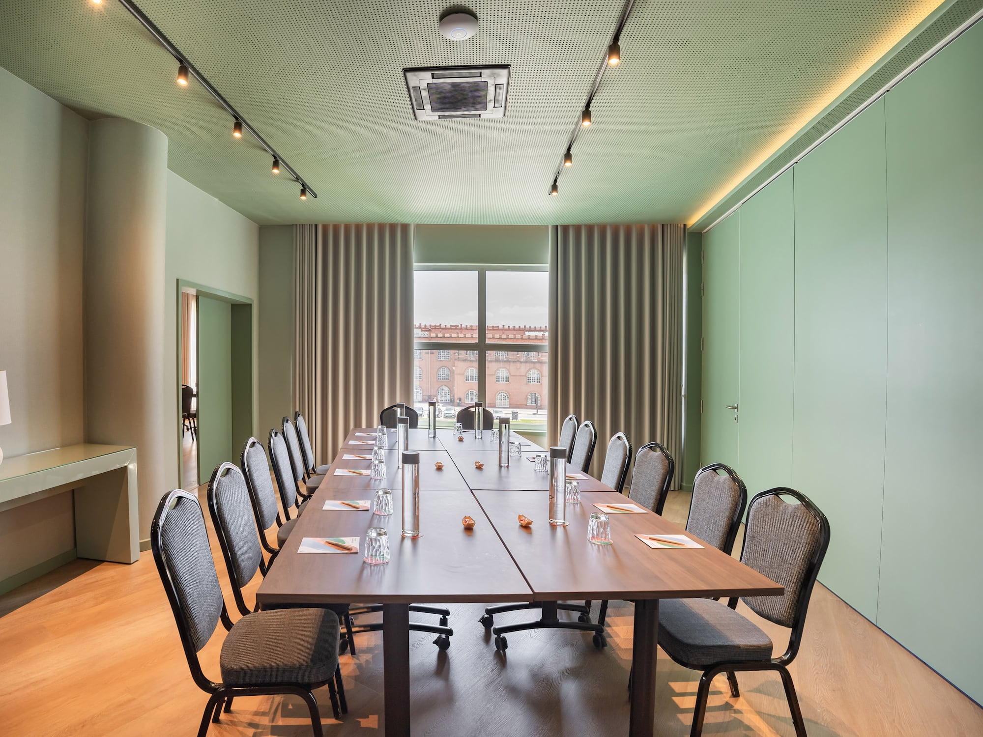 Modern green meeting room with long table, chairs, and city view from window.