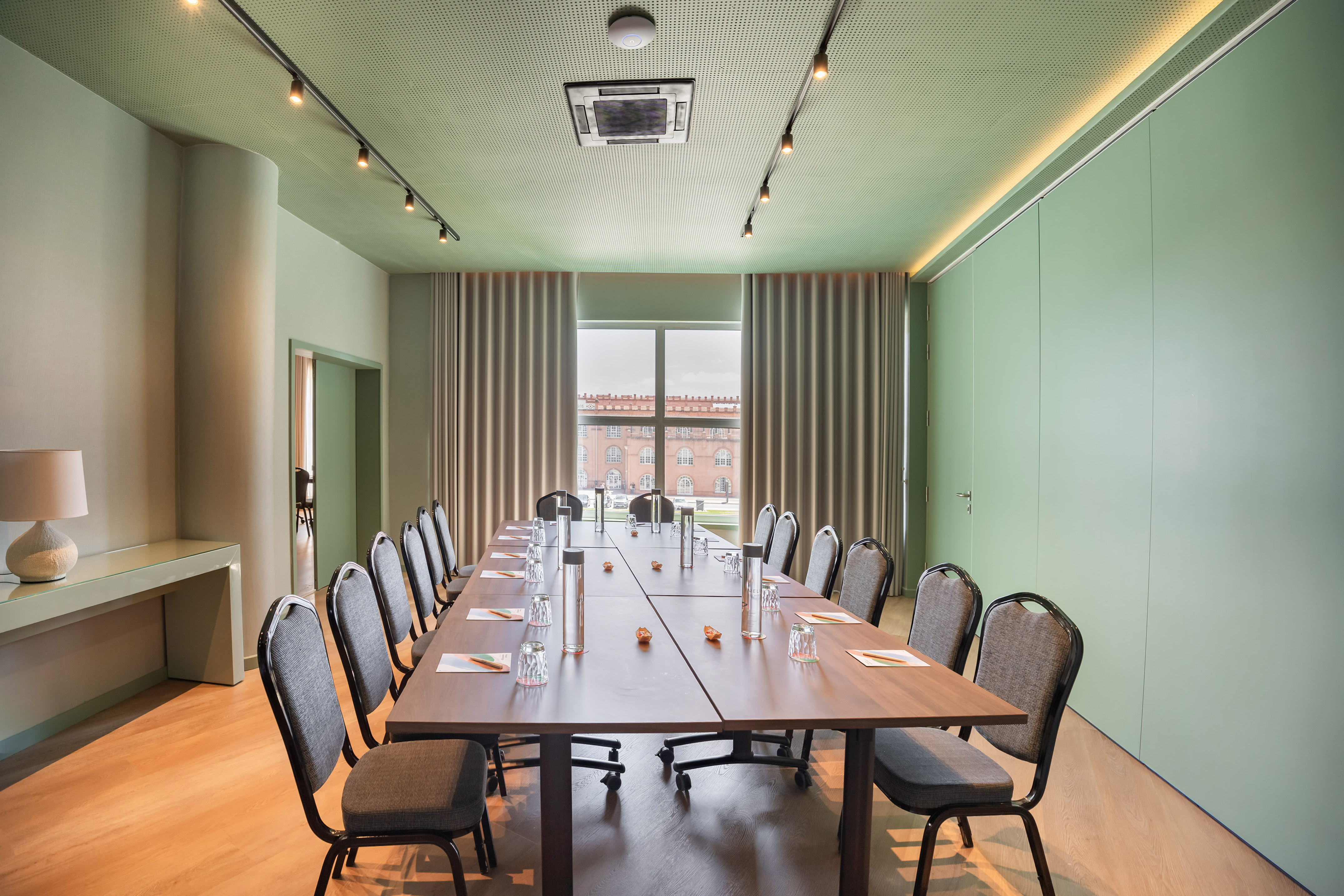 Modern green meeting room with long table, chairs, and city view from window.