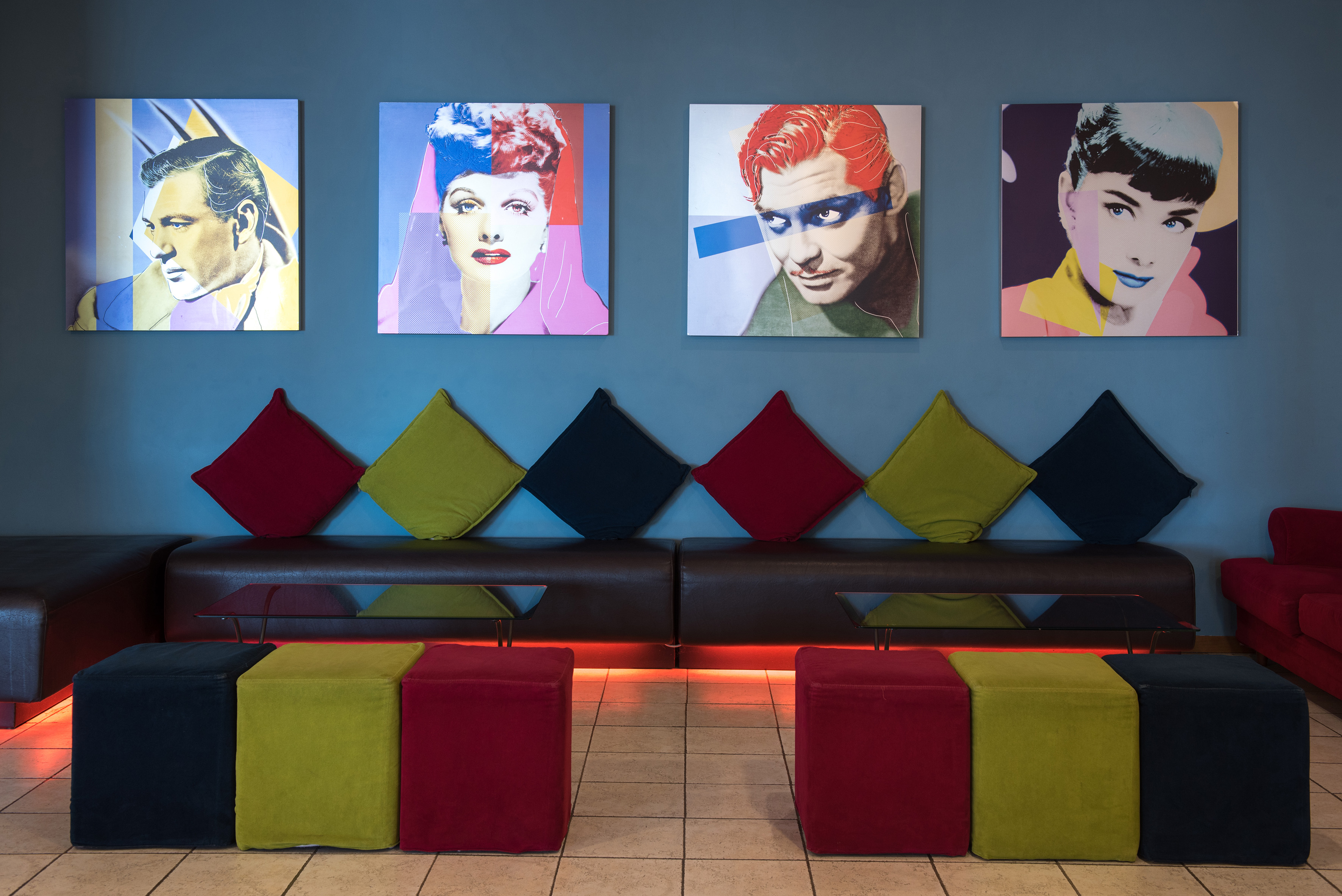 Modern lounge with pop art celebrity portraits, brown sofa, and colorful seating.
