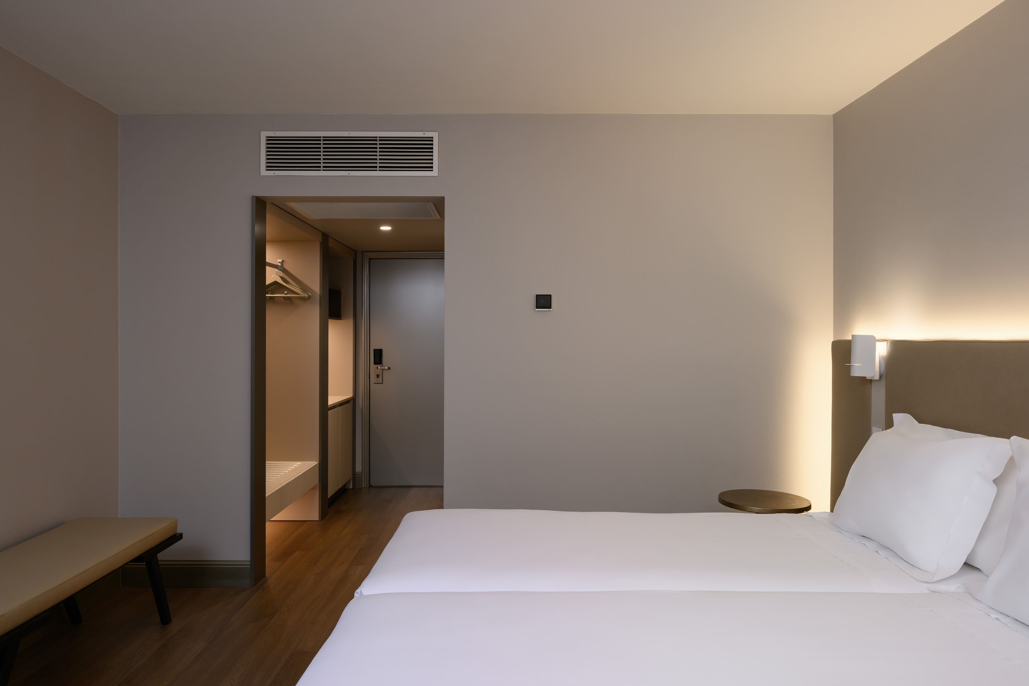 Modern hotel room with twin beds, lighted headboard, and open closet.
