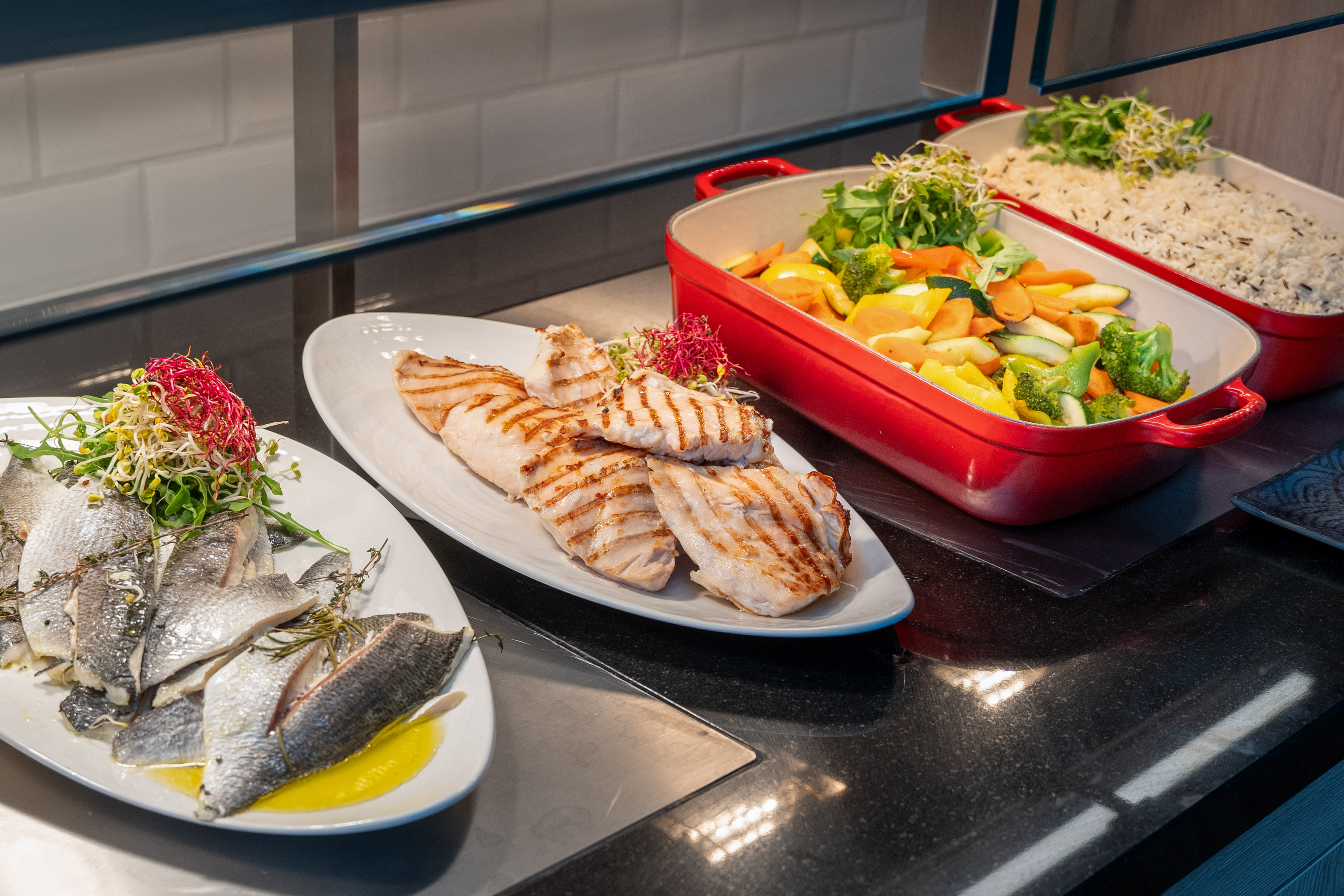 Healthy buffet with grilled chicken, fish fillets, roasted vegetables, and rice.