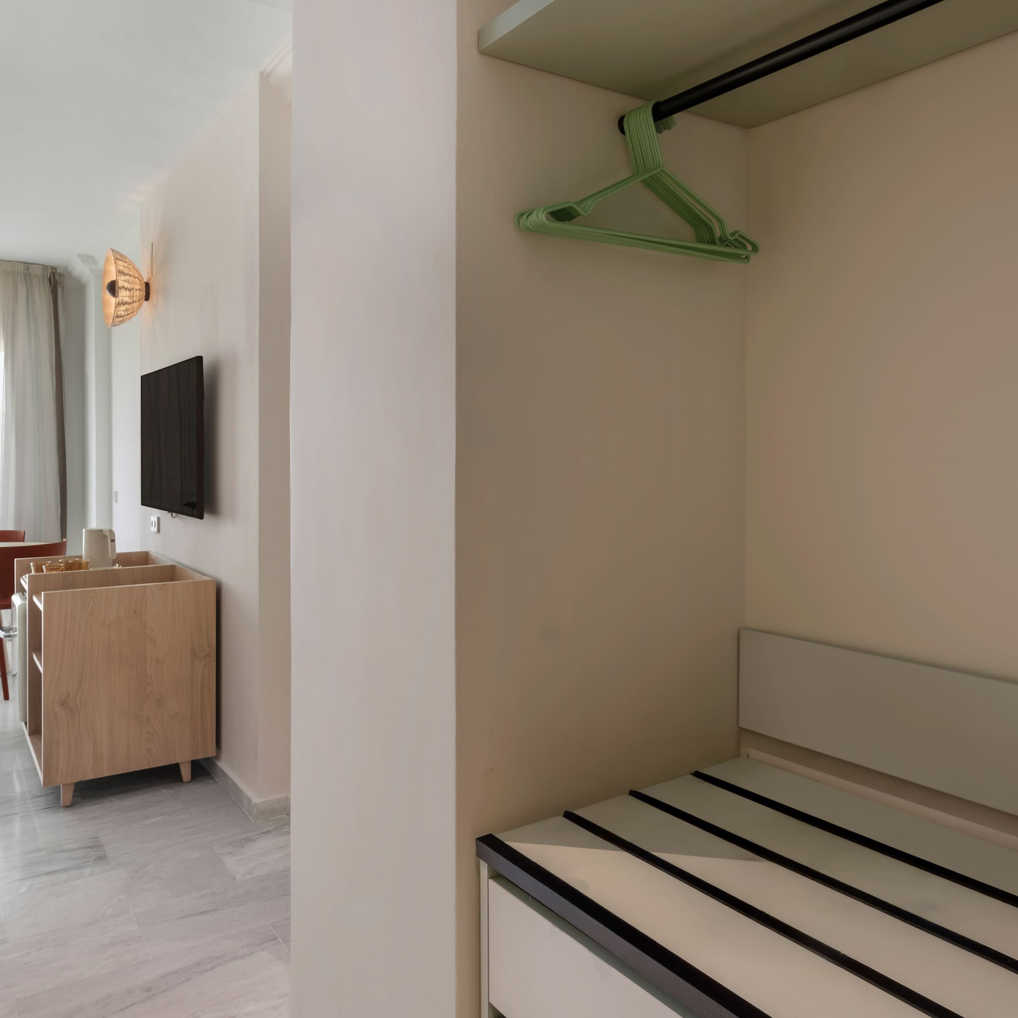 Hotel suite with open closet, green hangers, luggage rack, and bright living/dining area.