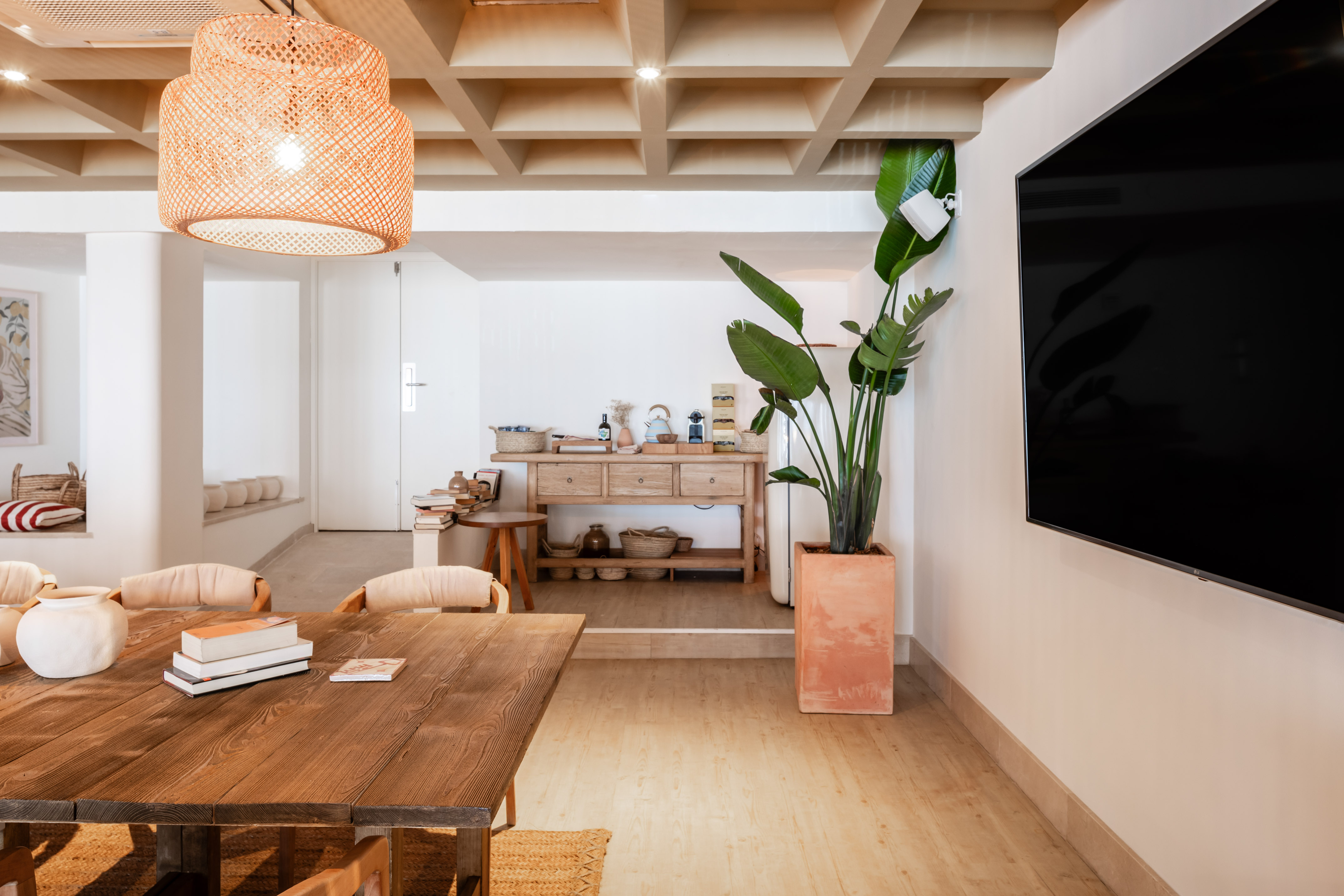 Modern dining room with wooden table, rattan light, large plant, and wall TV.